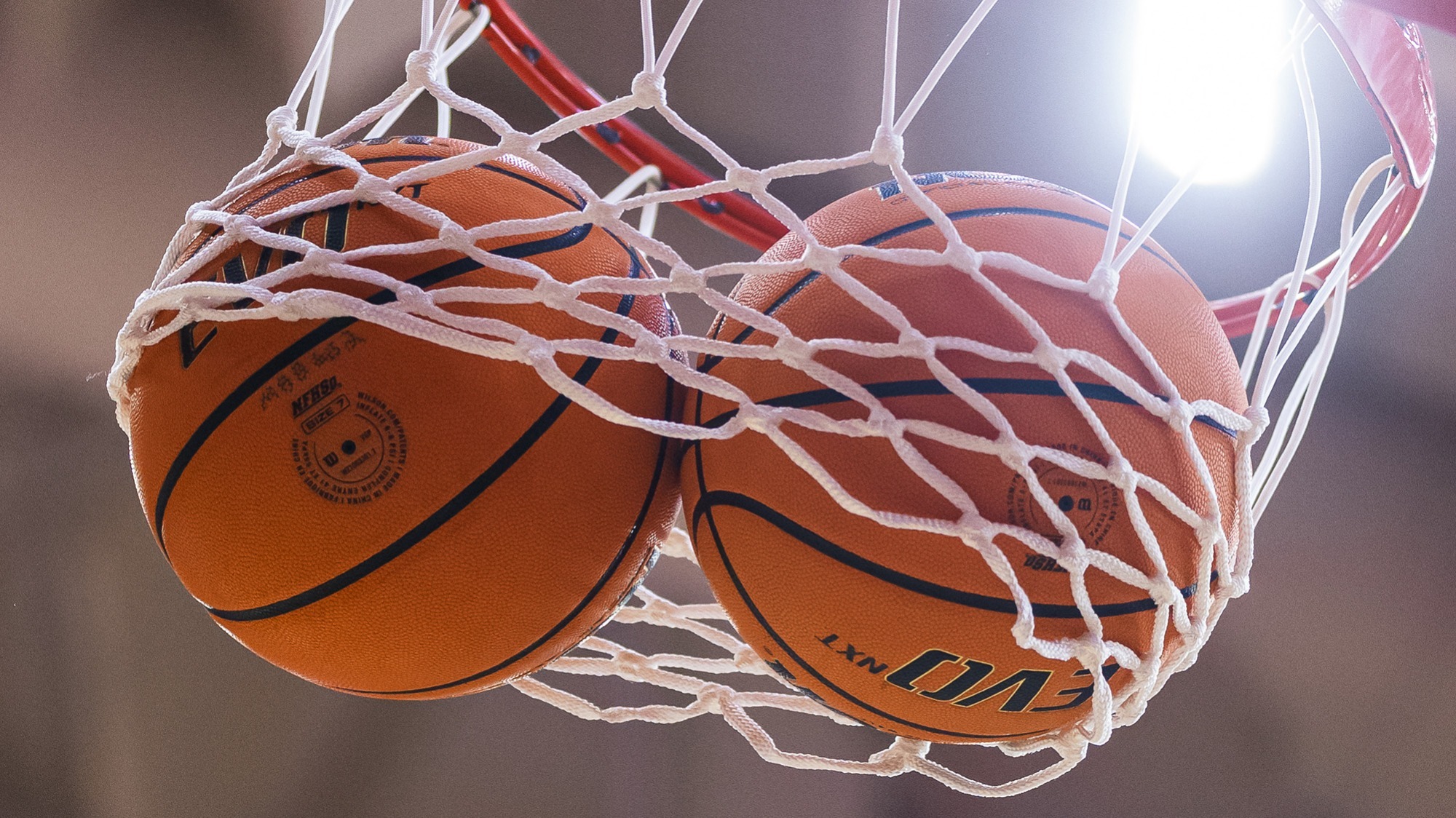 Two basketballs going through the net of a hoop.