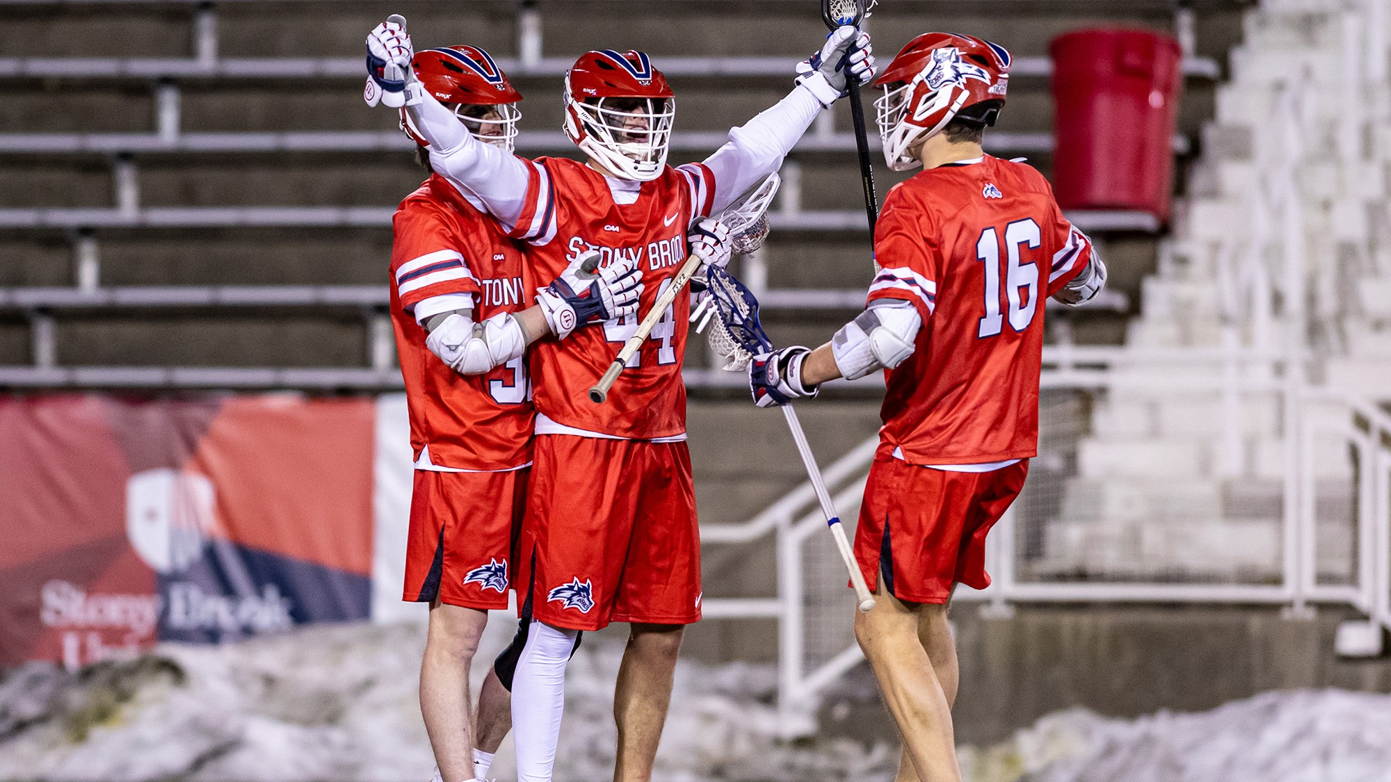Stony Brook men's lacrosse players Kian McCoy, Justin Bonacci and Collin Williamson celebrate together on the turf at LaValle Stadium.