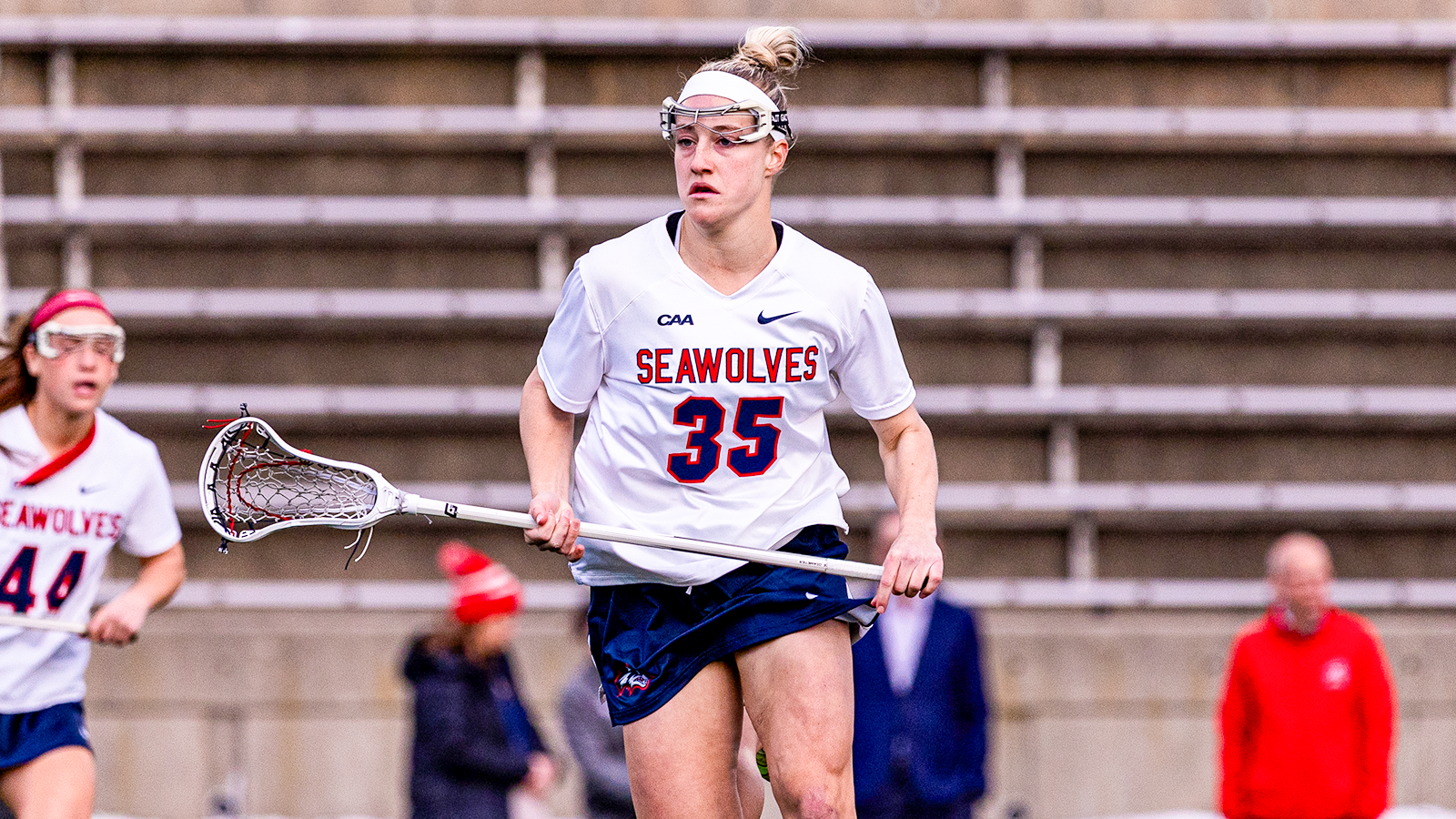 Isabella Caporuscio running down the field in a white and blue Stony Brook women's lacrosse uniform. 