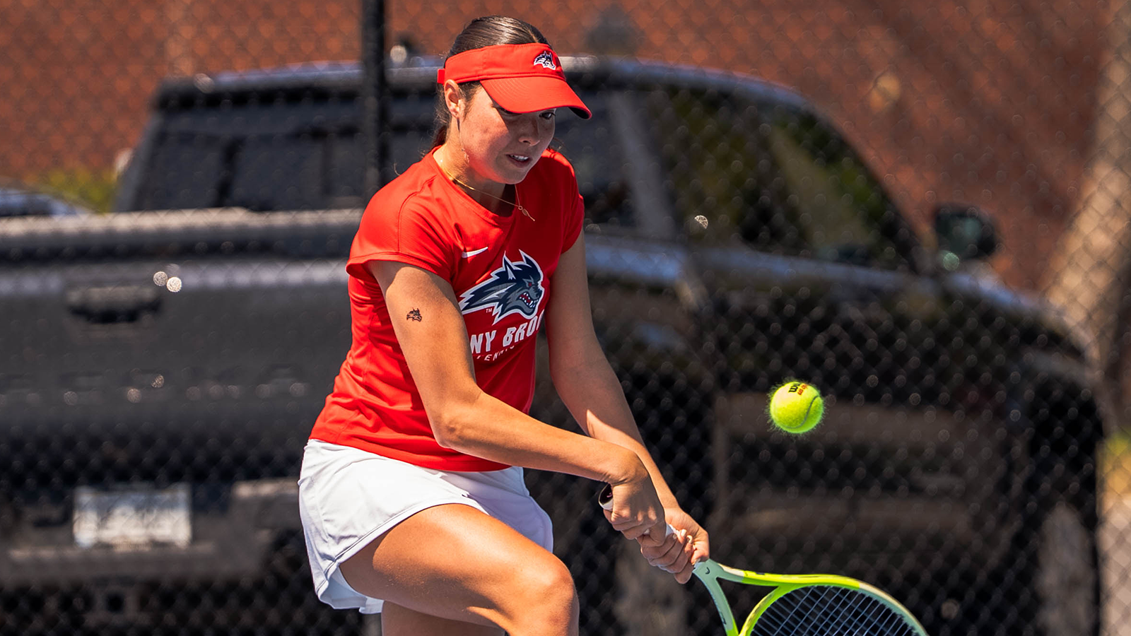 Elena Lobo-Corral in a red stony brook tennis uniform getting in position to hit a tennis ball. 