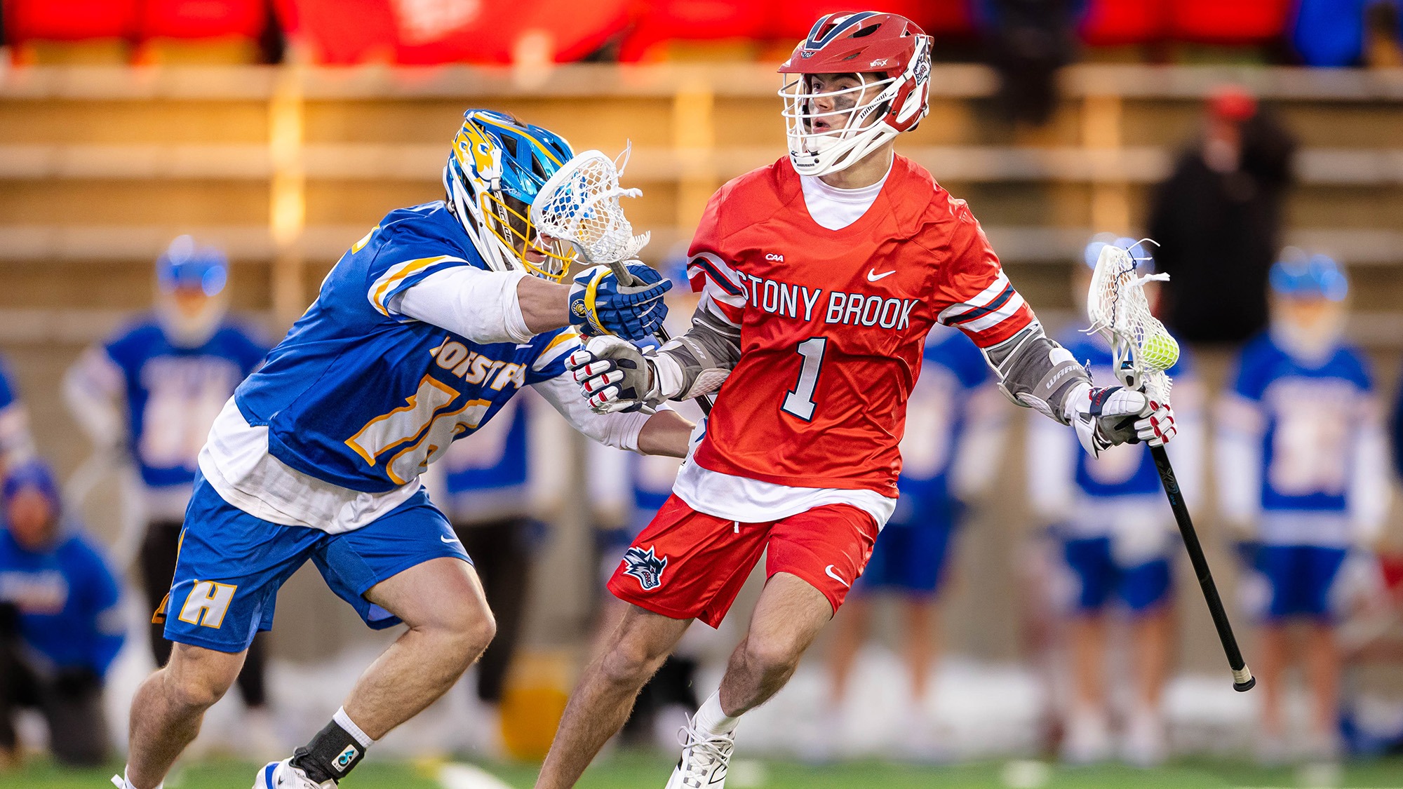 Stony Brook's Owen Donnellan in action, holding a lacrosse stick in his left hand while fending off a Hofstra defender.