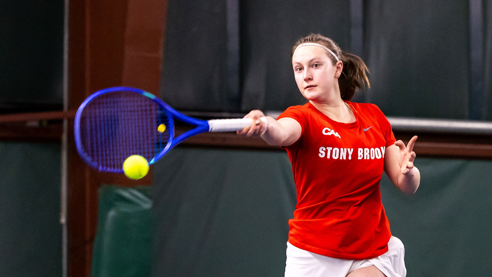 Stony Brook tennis player Laura Ozola hitting a tennis ball back to her opponent with her blue tennis racket. 
