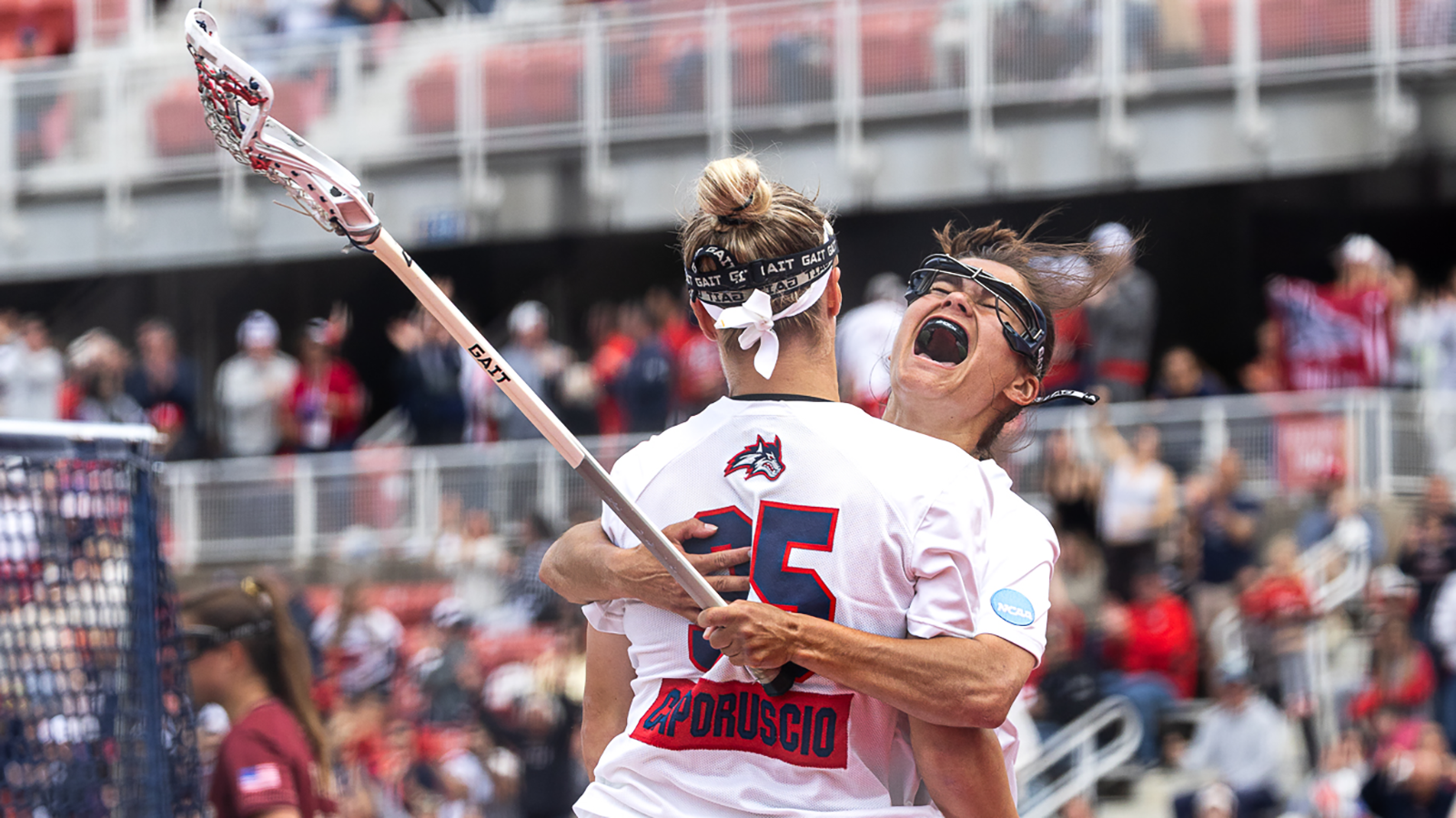 Stony Brook women's lacrosse players Isabella Caporuscio, and Katie Walsh hug and celebrate a goal scored.