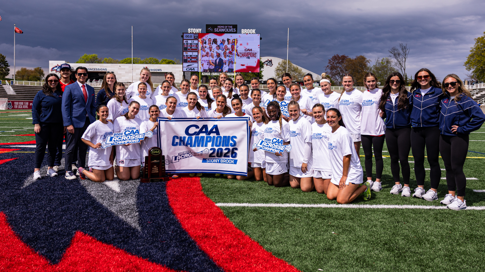 The Stony Brook women's lacrosse team poses for a team picture with the CAA Championship trophy and banner.
