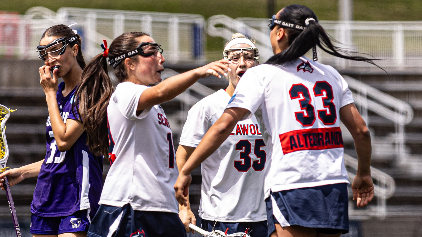 Stony Brook women's lacrosse players Julia Fusco, Mirabella Altebrando, and Isabella Caporuscio huddle around each other and celebrate after a goal scored.