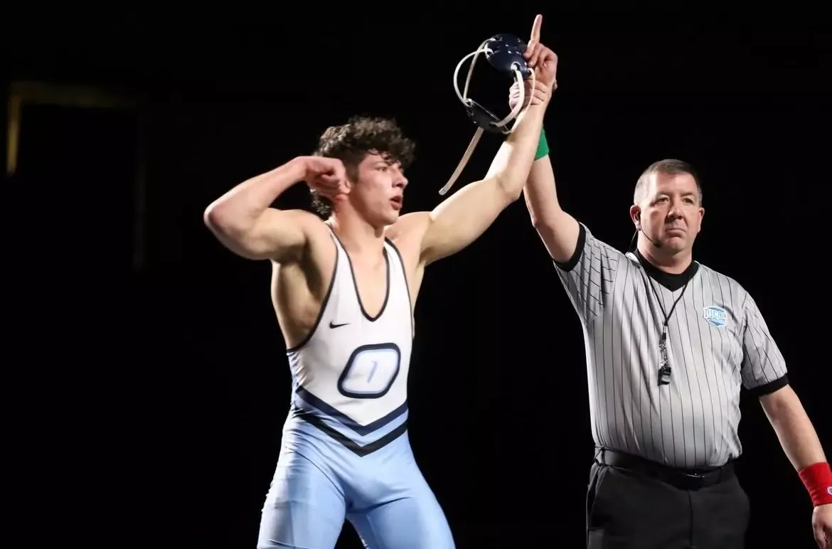 A victorious wrestler in a light blue singlet with a bold 