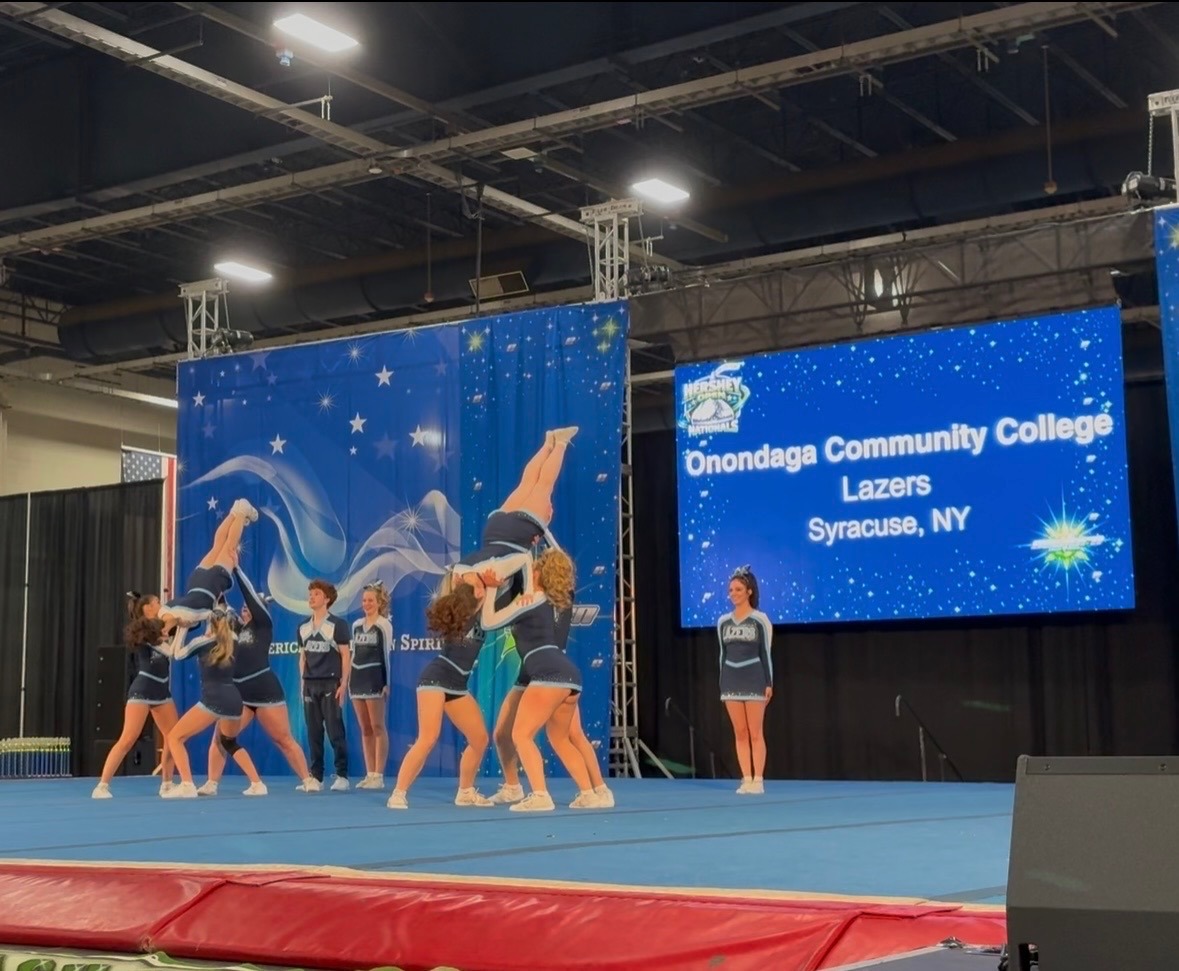 Cheerleading team performing a complex lift with precision on a blue mat. A sign reads 