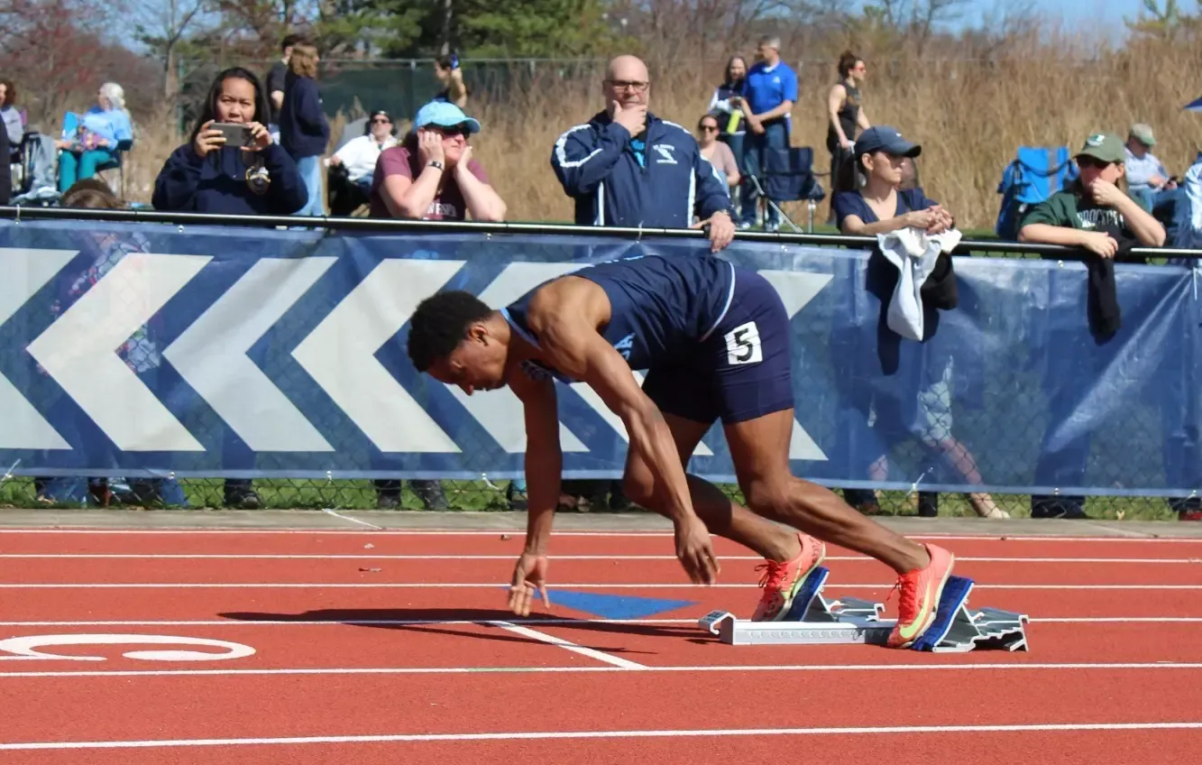 An athlete in a navy uniform and bright sneakers starts at a race track.