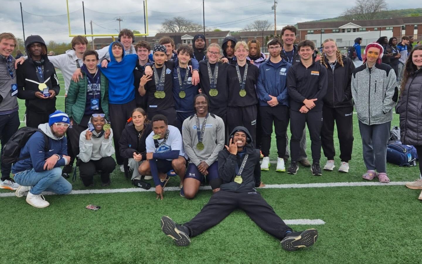 A group of smiling athletes wearing medals poses on a field under a cloudy sky. Their expressions convey a sense of achievement and camaraderie.