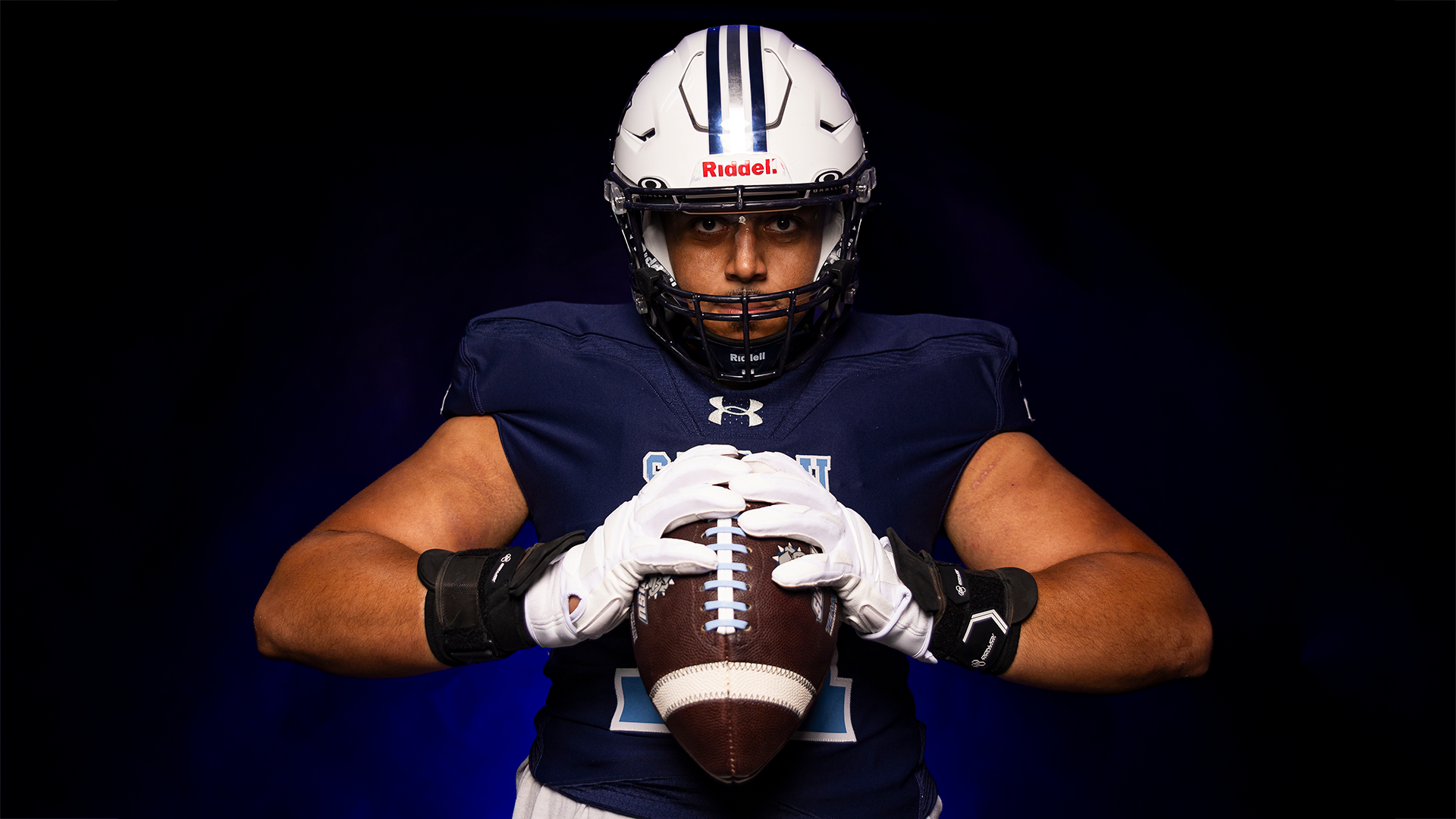 Jason Dennis squeezes a football with two hands in a posed shot