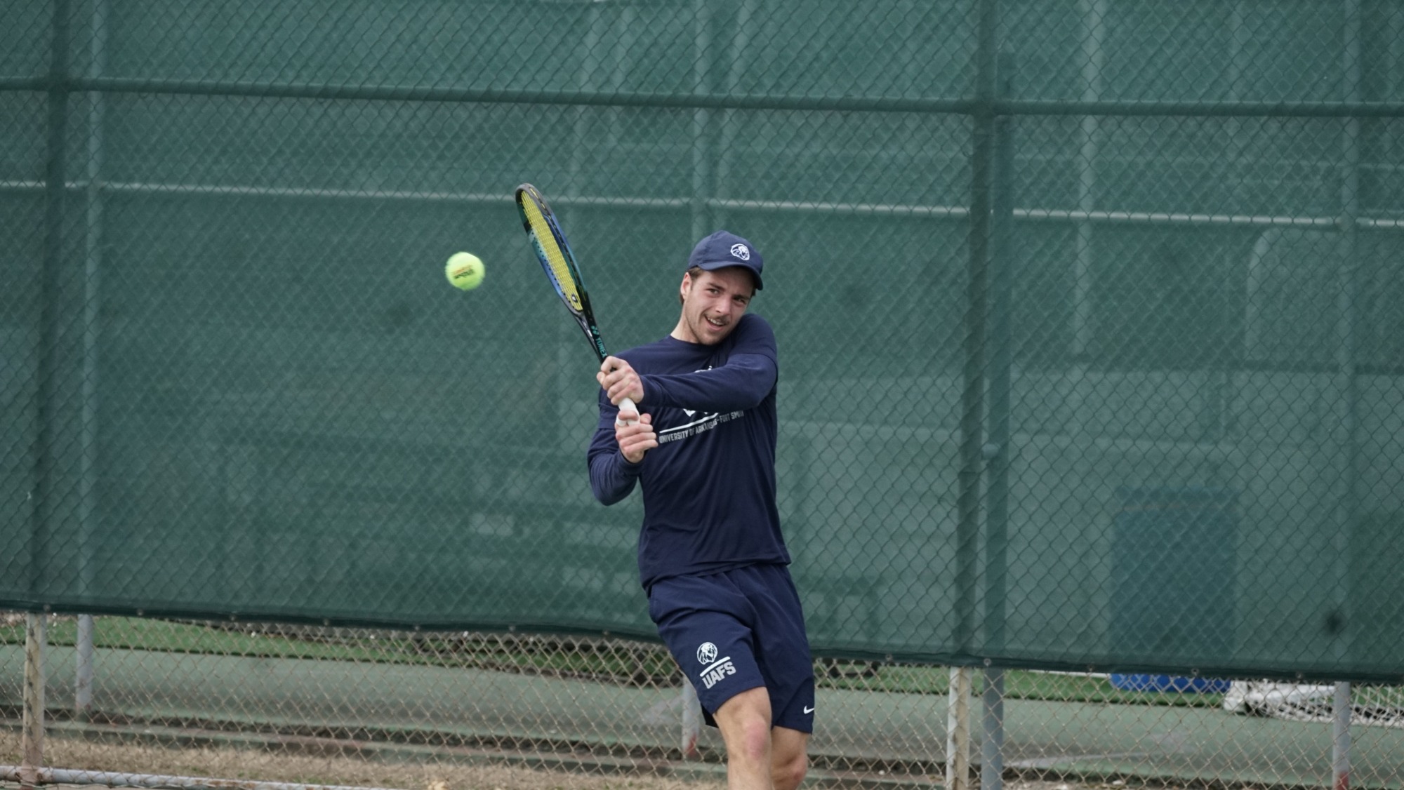 A men's tennis player wearing a blue shirt returns a shot during a match. 