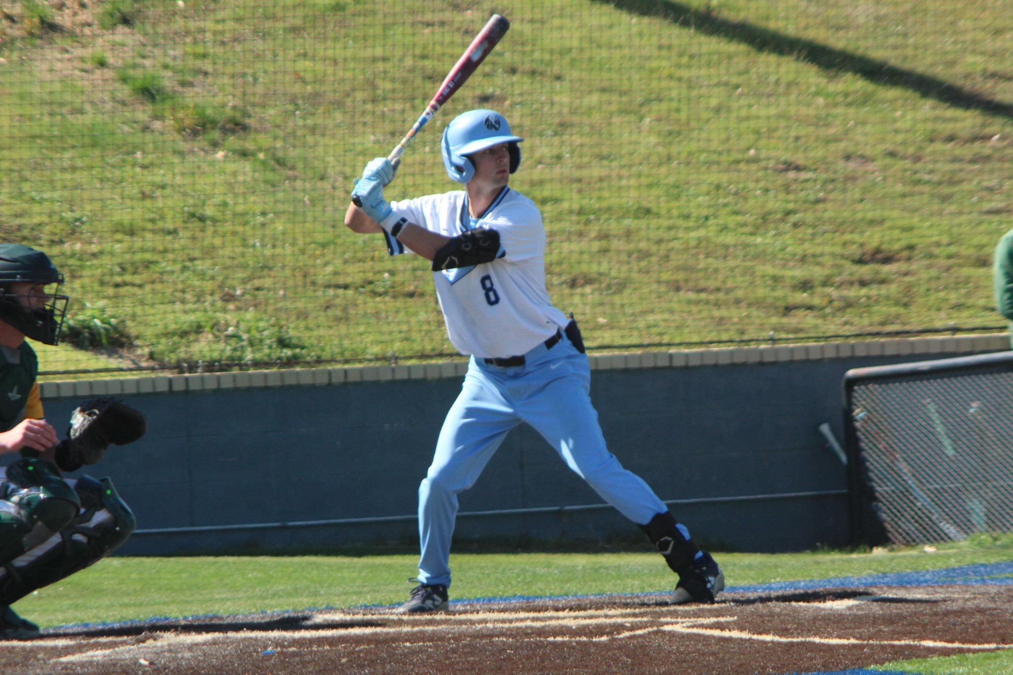 A baseball player in his batting stance with a blue helmet, white jersey and blue pants. 