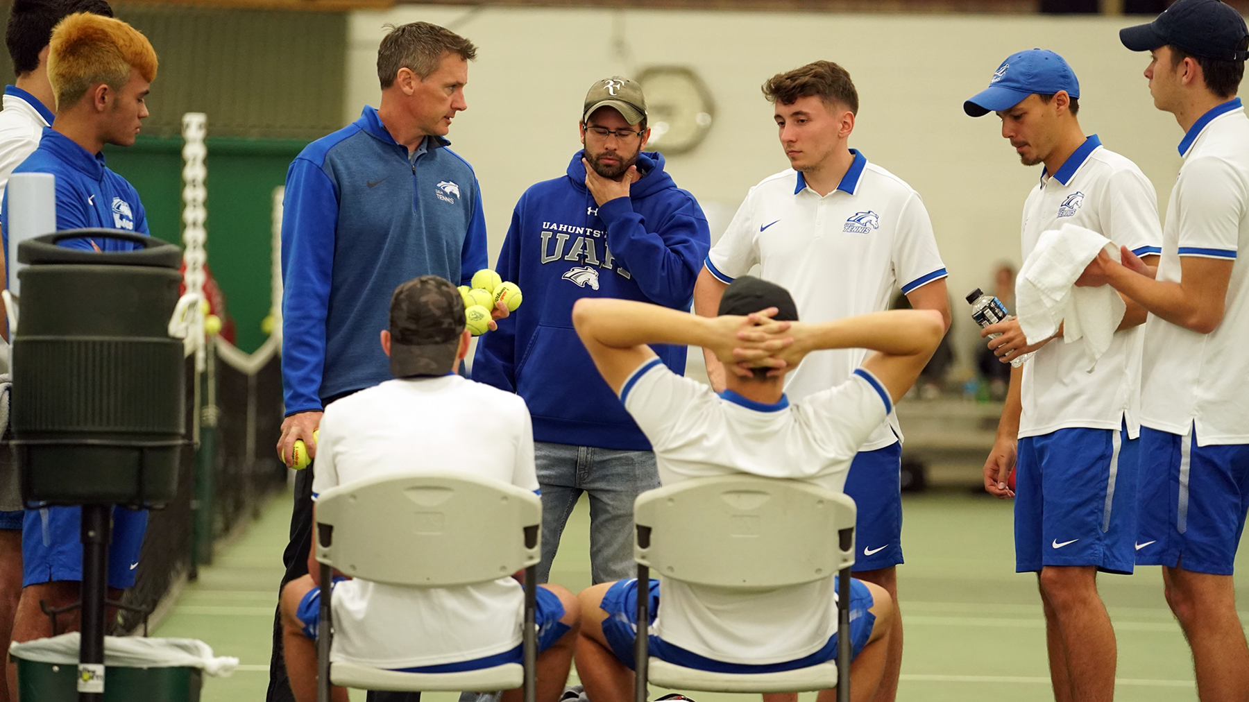 The men's tennis team listens to Coach Thomson.
