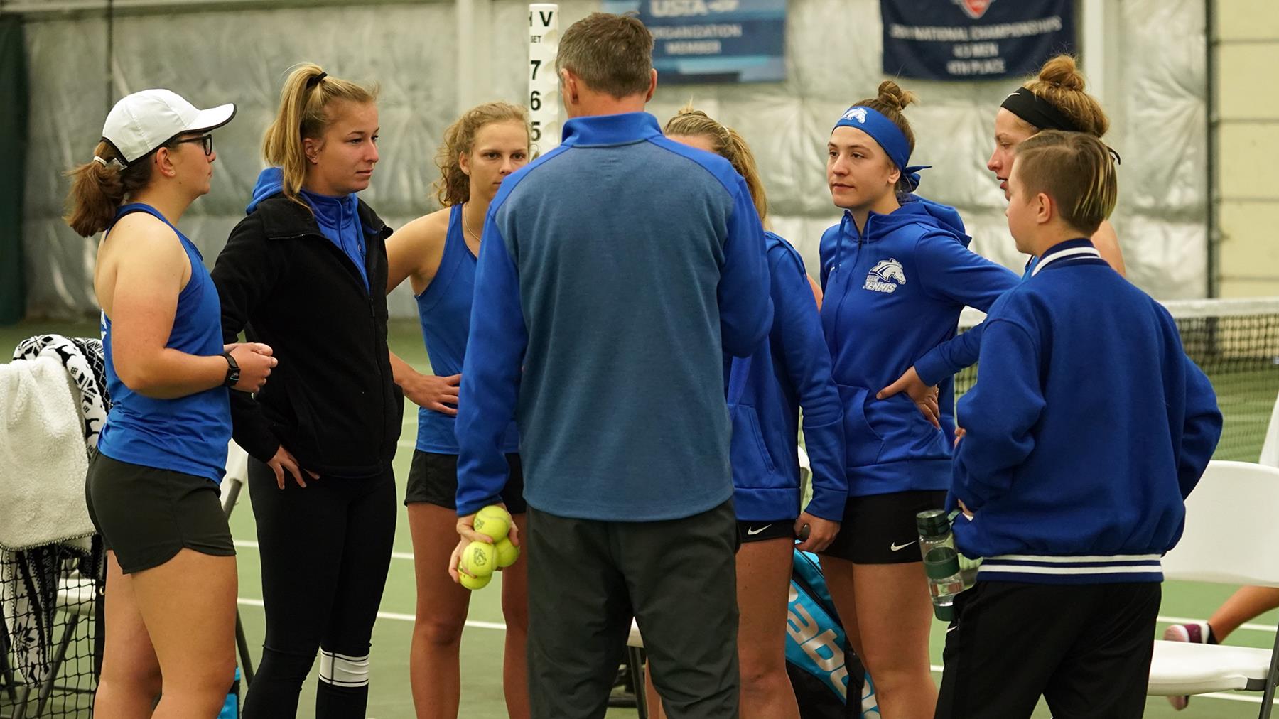 The women's tennis team listens to Coach Thomson.