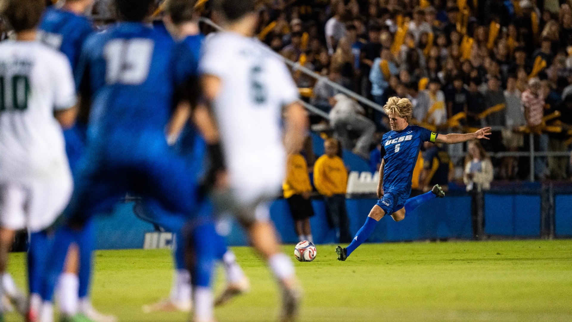 #6 Kalle Rahbek winds up to take a free kick against Cal Poly. Teammates and opponents jostle for position out of focus in the foreground.