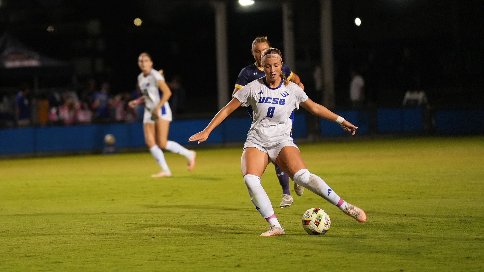 Regan Stiner (#8) gets ready to pass the soccer ball to a player with a defender on her back.