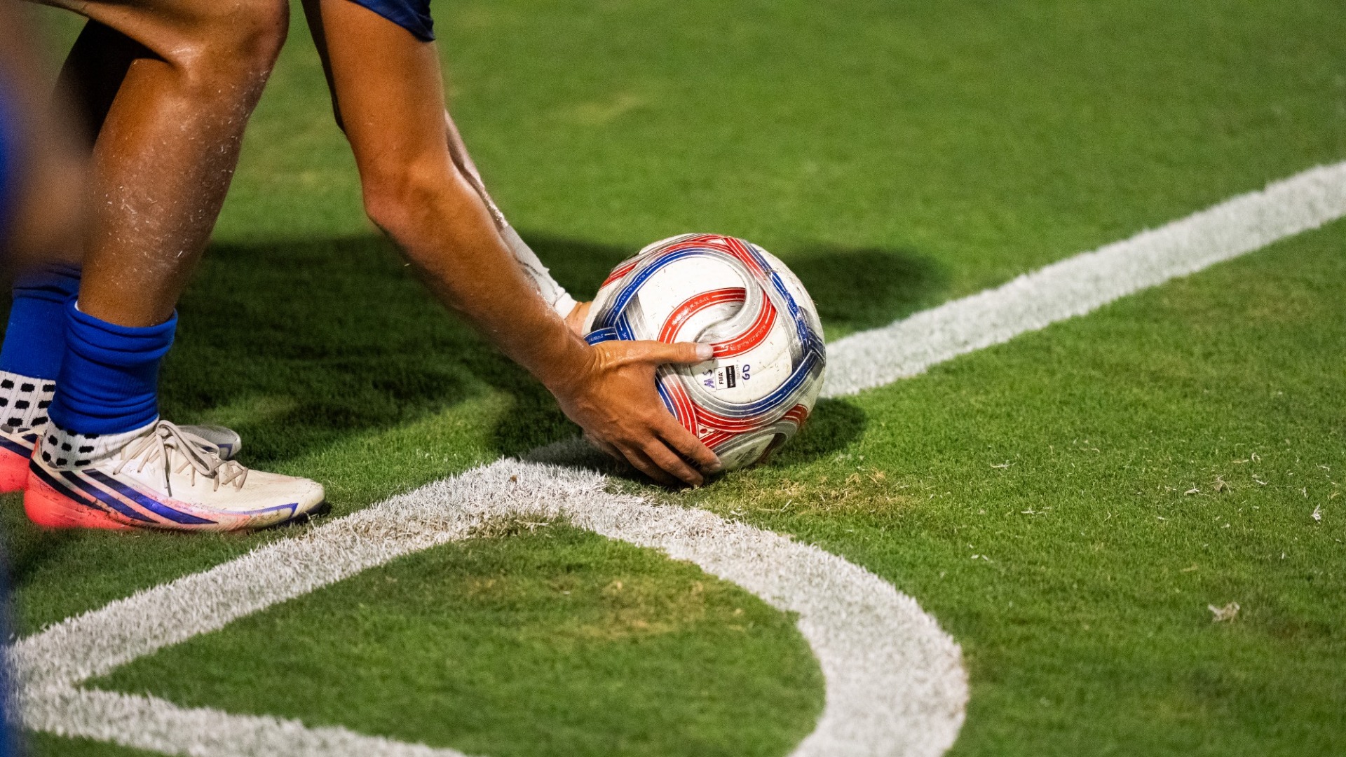 A soccer player's arms and legs are visible in the upper left quarter of the frame as he places a ball on the corner arc