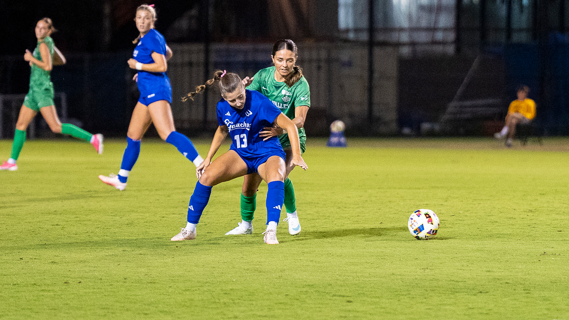 Caitlyn Simons (#13) battles with a Utah Valley midfielder to gather possession of a loose ball. 