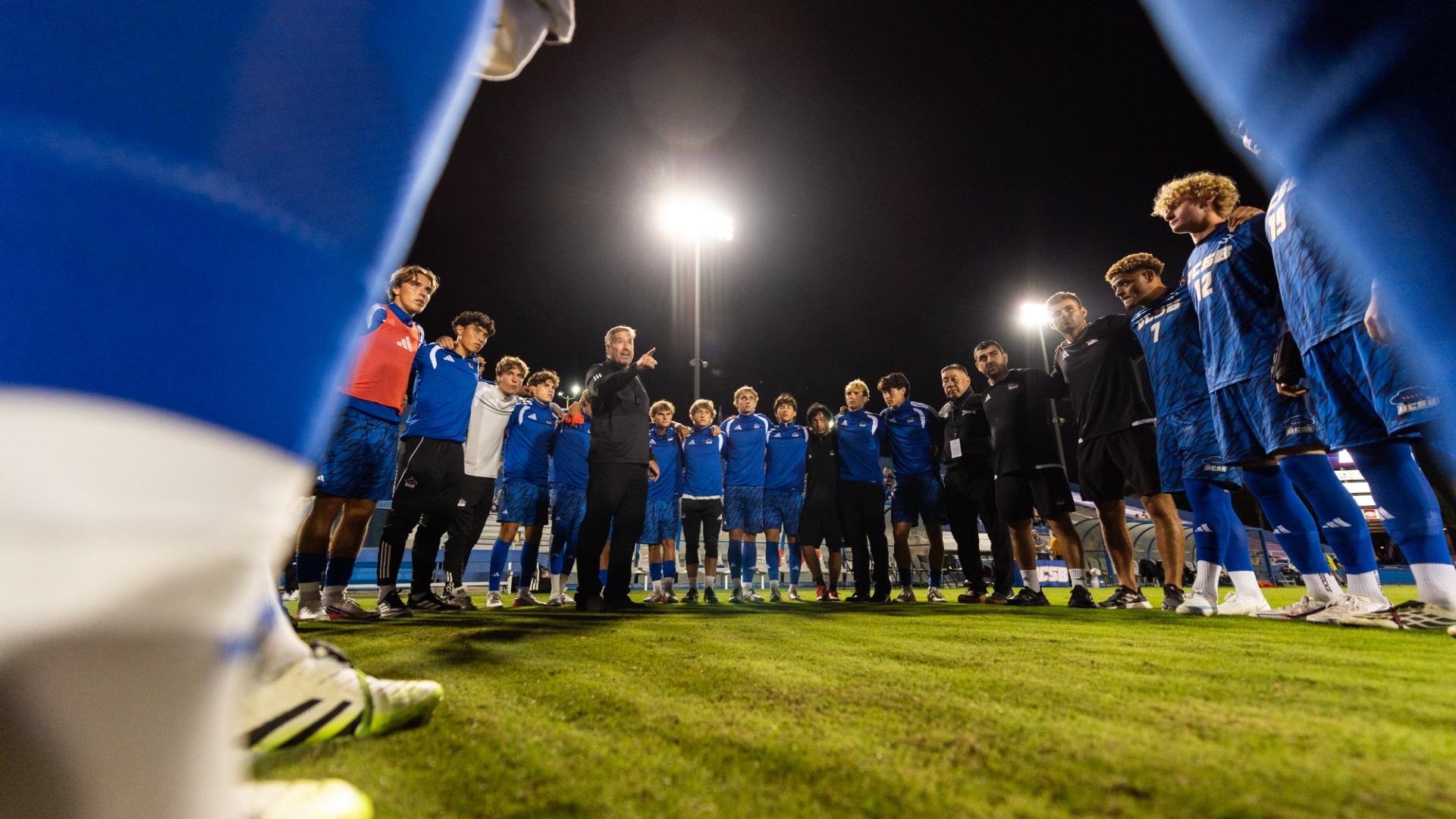 Head coach Tim Vom Steeg gives instructions as the UC Santa Barbara Men's Soccer team surrounds him in a large circle, their arms draped around each others' shoulders