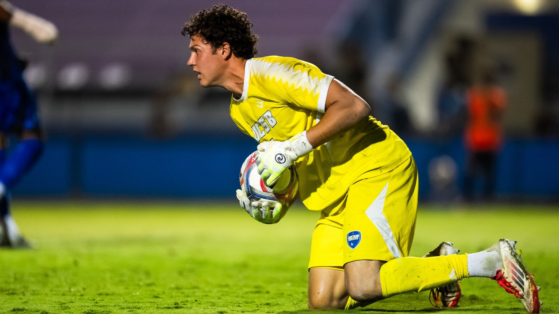 A profile view of #1 Owen Beninga, who appears hunched over as he makes his way up from a kneeling position with a ball wrapped in his arms, under his chest