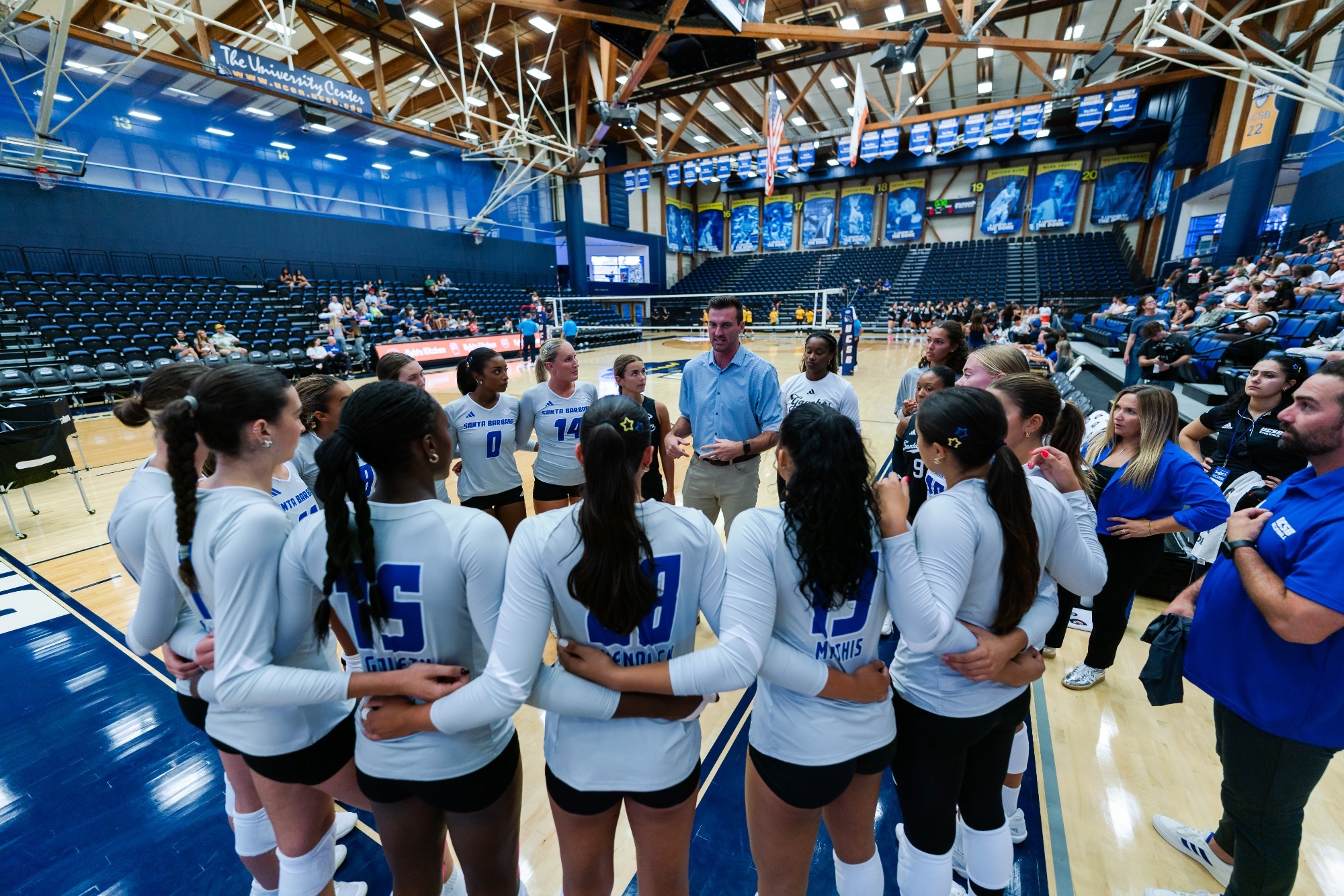 Group shot of women's volleyball in a circle while Head Coach Mike Henchy talks to them