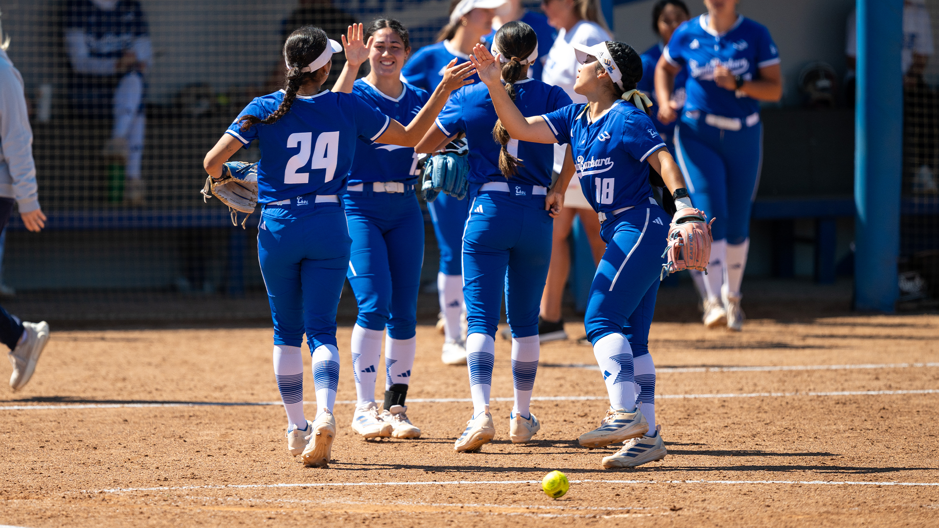 Jaelyn Toledo (#24) and Bella Fuentes (#18) give each other a high-five after a defensive inning in the field. behind them, Ella Myers (#13) and Tehya Banks (#1) are also celebrating with a high-five.
