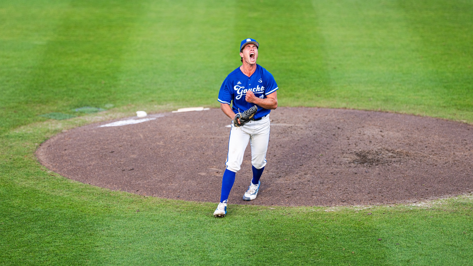Cole Tryba (#7) lets out a triumphant yell as he walks off the pitching mound. His arms are flexed low in front of him as he throws his head back and roars in celebration.