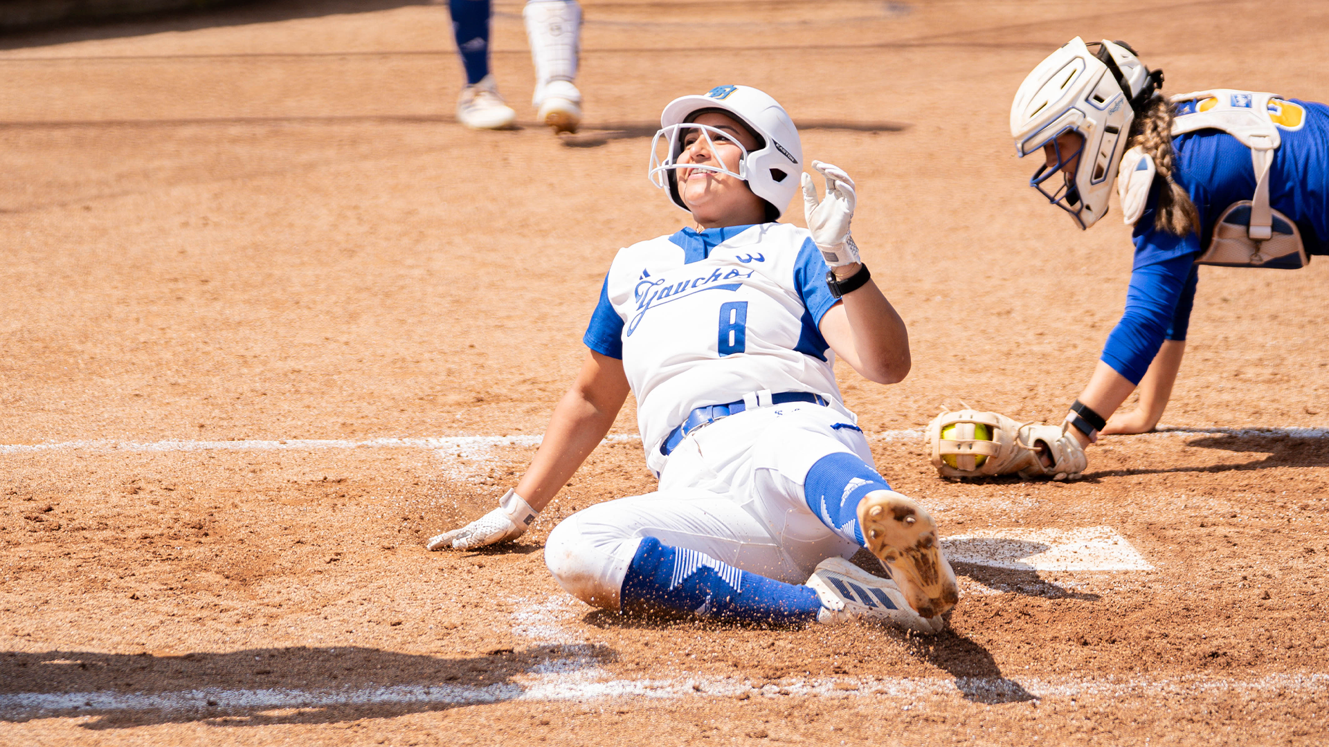 #8 Giselle Mejia slides in to home plate past the catcher swiping a tag as she looks up for the umpires call.