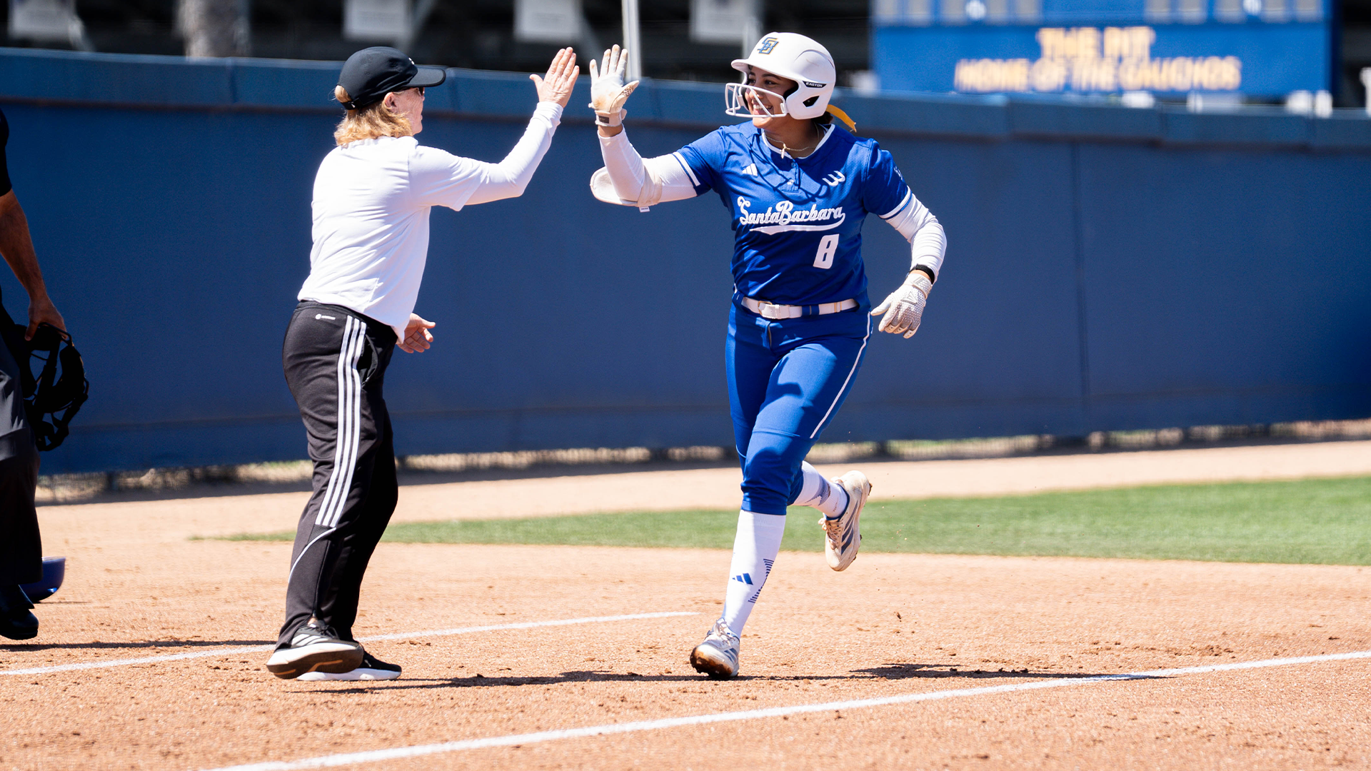 #8 Giselle Mejia rounds third and gives a high-five to Head Coach Jo Evans after hitting a home run in the first inning of the game.