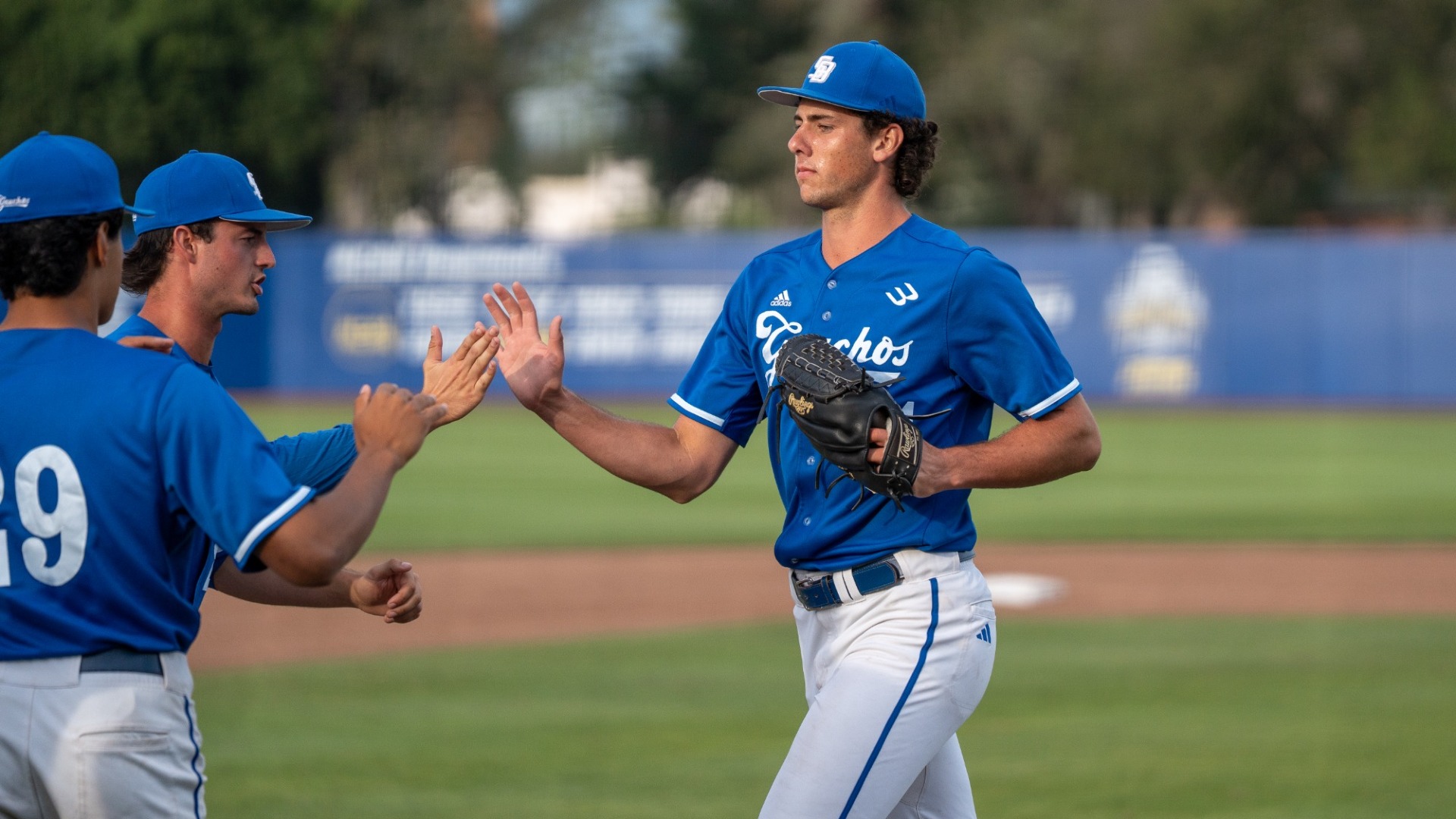 Stunner Gonzales (#34) receives high-fives from his teammates on the way back into the Gauchos' dugout. His expression is stoic and calm, like pitching is easy.