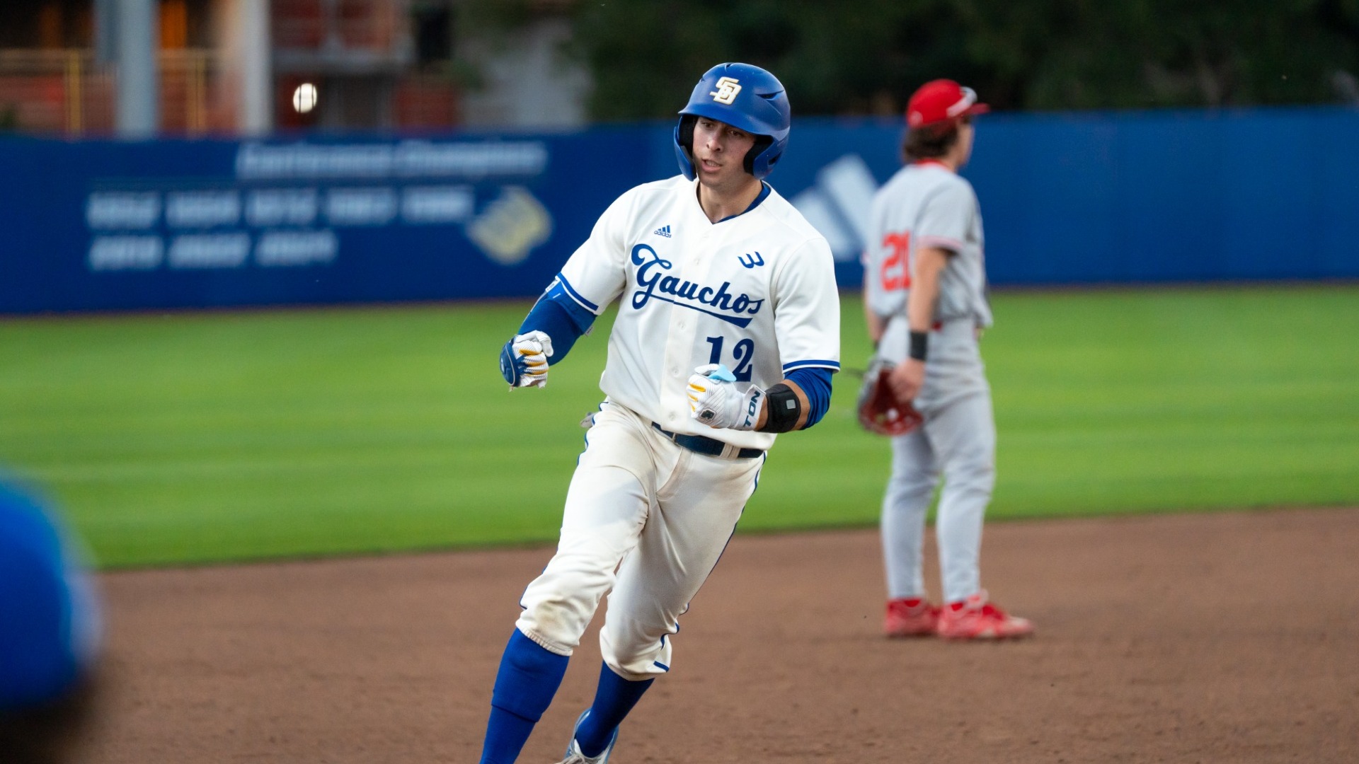 Nate Vargas (#12) rounds third base after his home run against Utah. He is pumping both fists in front of his midsection in celebration.