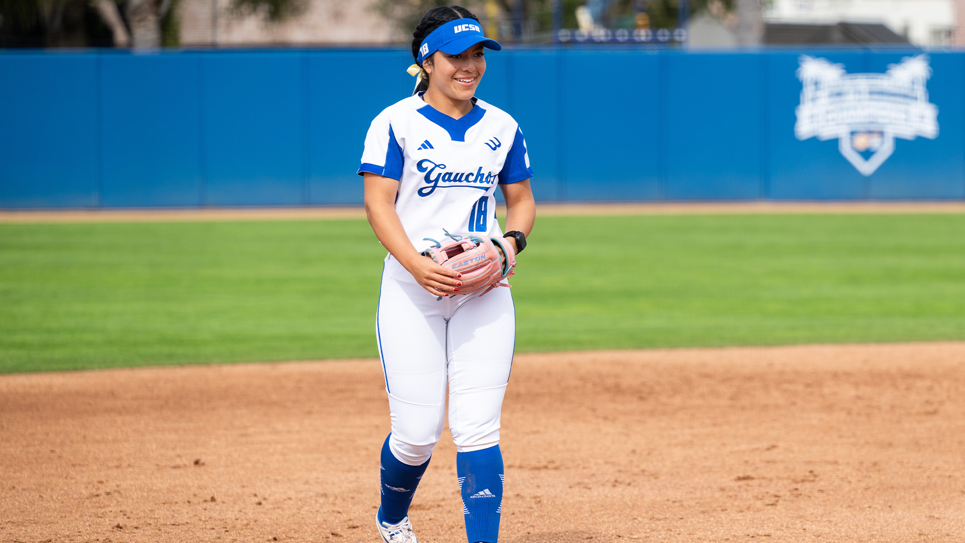 Bella Fuentes (#18) stands smiling at third base after making a play with her throwing hand over her glove. 