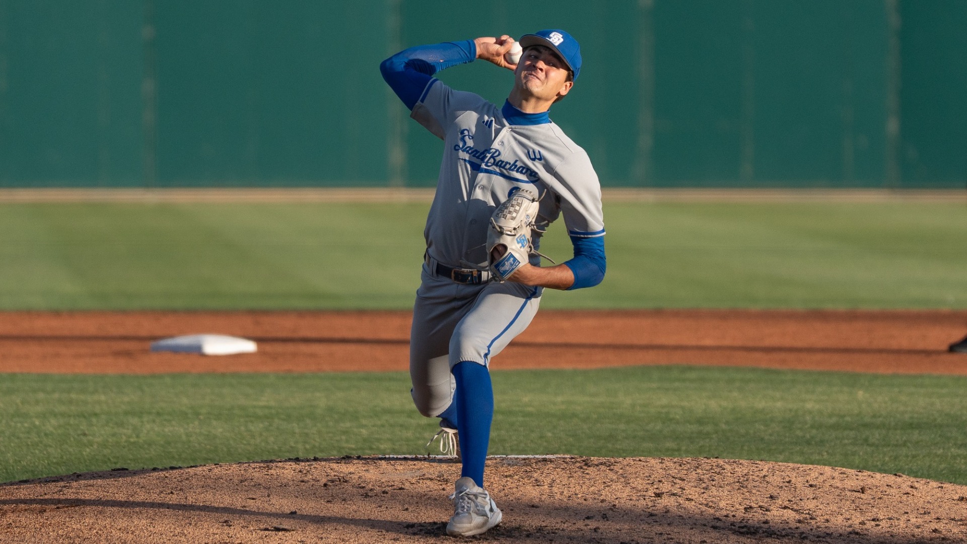 Jackson Flora (#2) delivers a pitch against Cal Poly. We are looking at him square on and can see that his shoulders and hips are square on to the camera as his right arm comes around from behind his head. The baseball in his hand is still partially blocked from our view. 