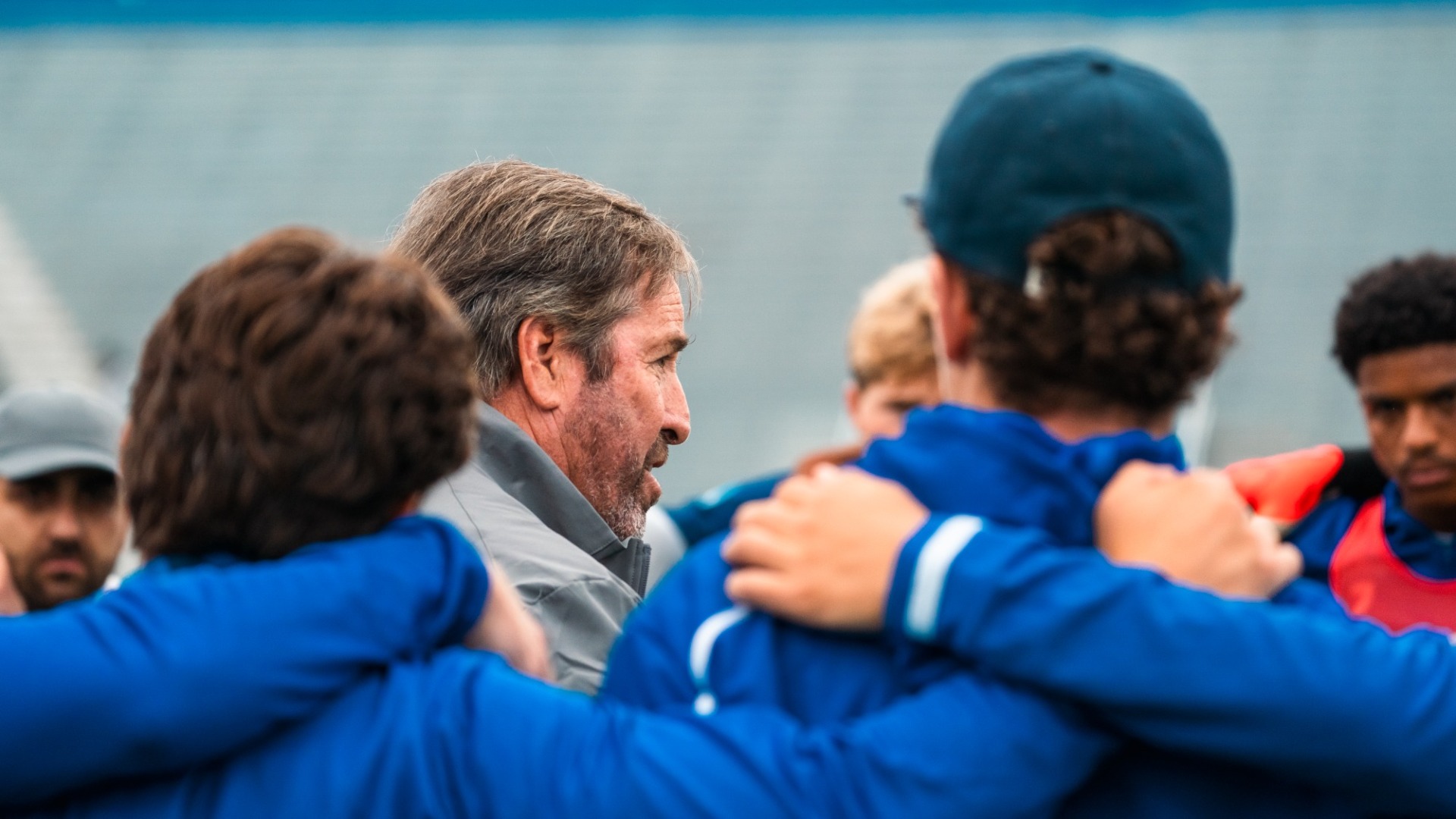 Tim Vom Steeg stands in the middle of a huddle of his players on a grey day. 