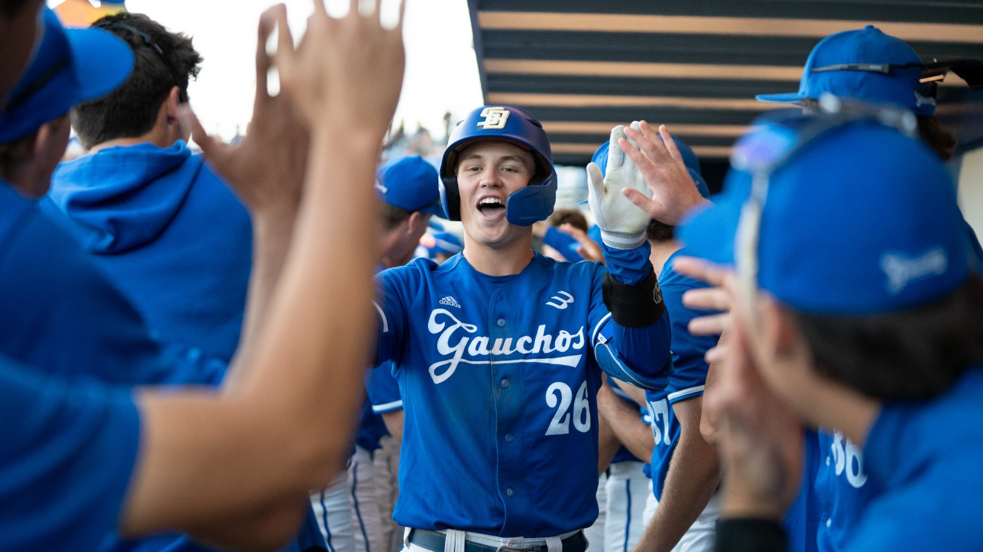 #26 William Vasseur flashes a big, wide smile as he high-fives teammates on either side of him in the dugout