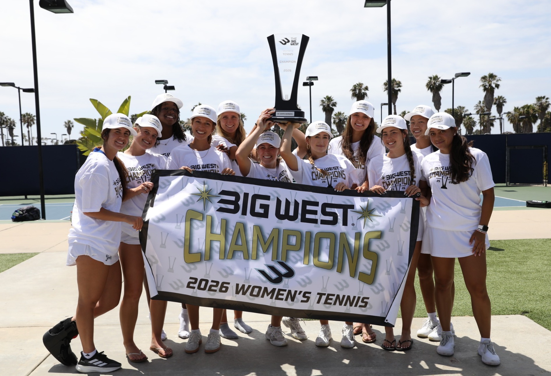 Women's Tennis holds trophy and banner, smiling after winning the Big West Championship back-to-back
