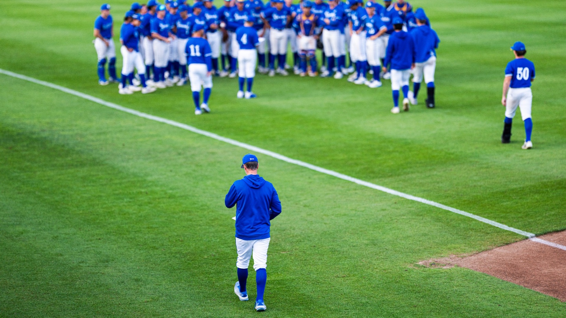 Andrew Checketts has his back to the camera as he walks towards his team postgame. The team stands in a semicircle, out of focus in the background