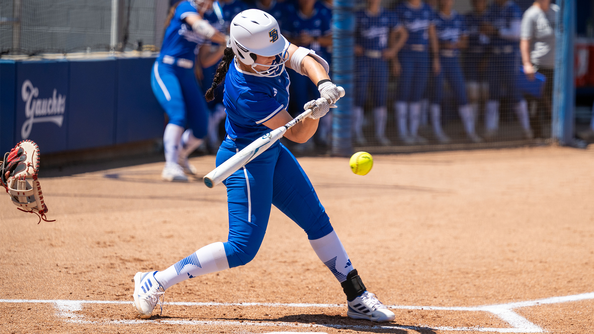 Ella Myers (#13) swings at an incoming pitch. She is mid way through her swing with the ball approaching her bat. 