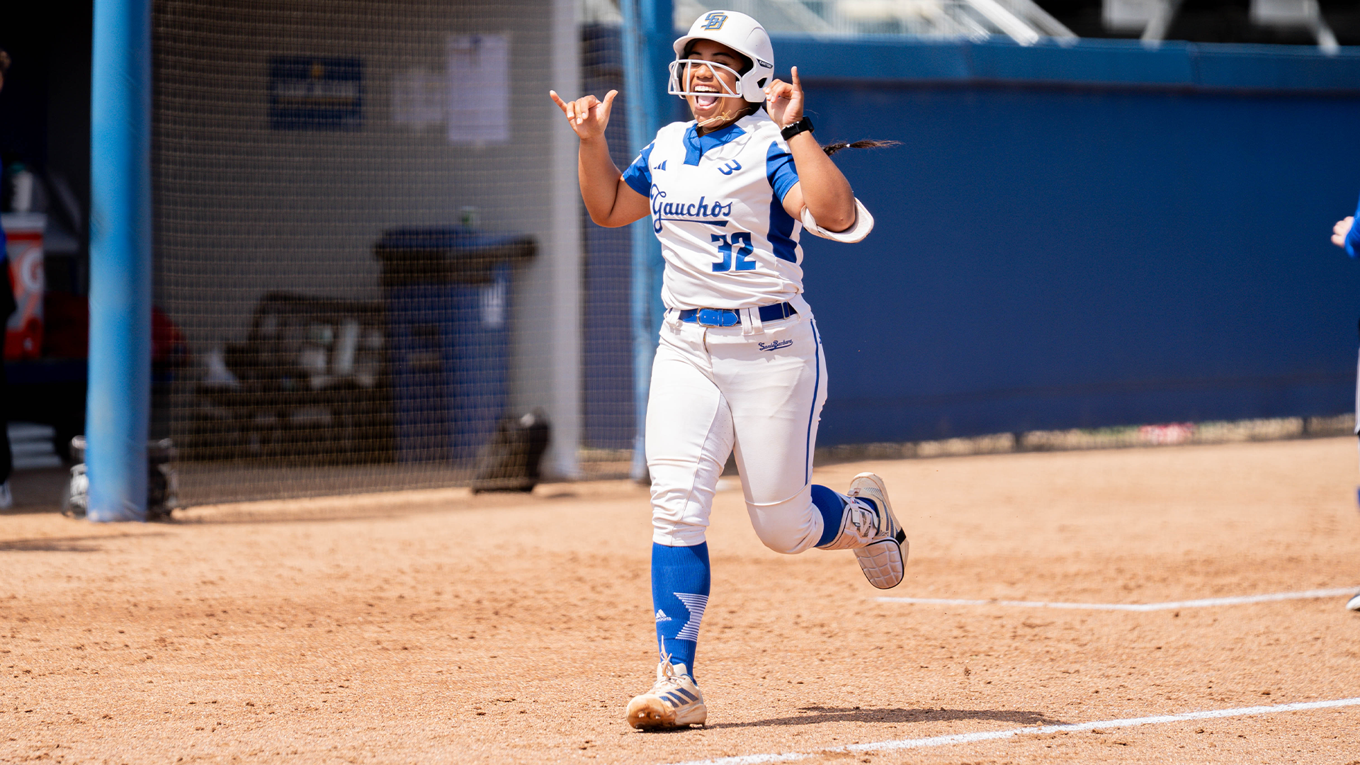 #32 Delaina Ma'ae celebrates one of her two home runs on the day against Hawai'i. Ma'ae is jogging home with her hands in a shaka sign smiling.