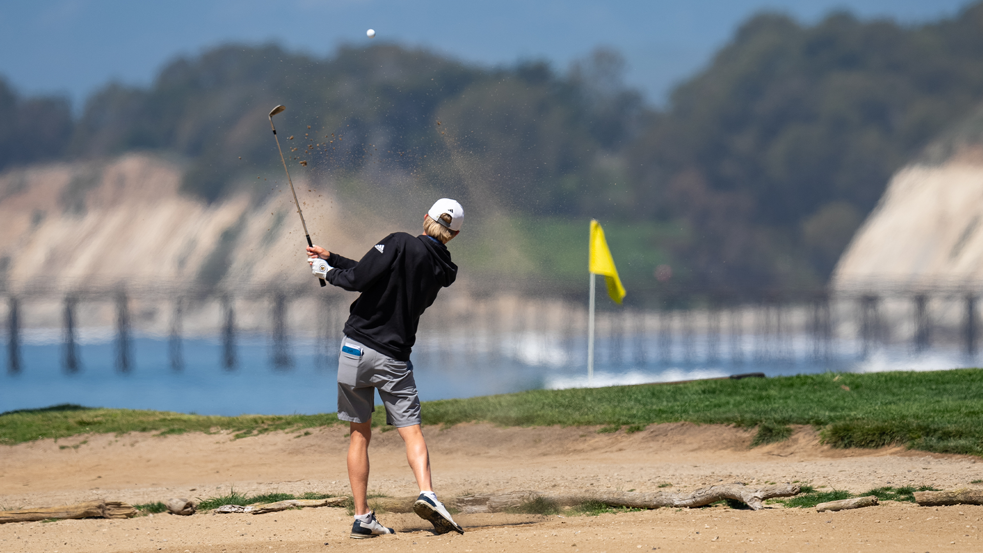 Ryan Gay finishes his swing out of the bunker as the ball is in the air traveling towards the flag stick on the par 11th hole at Sandpiper Golf Course.