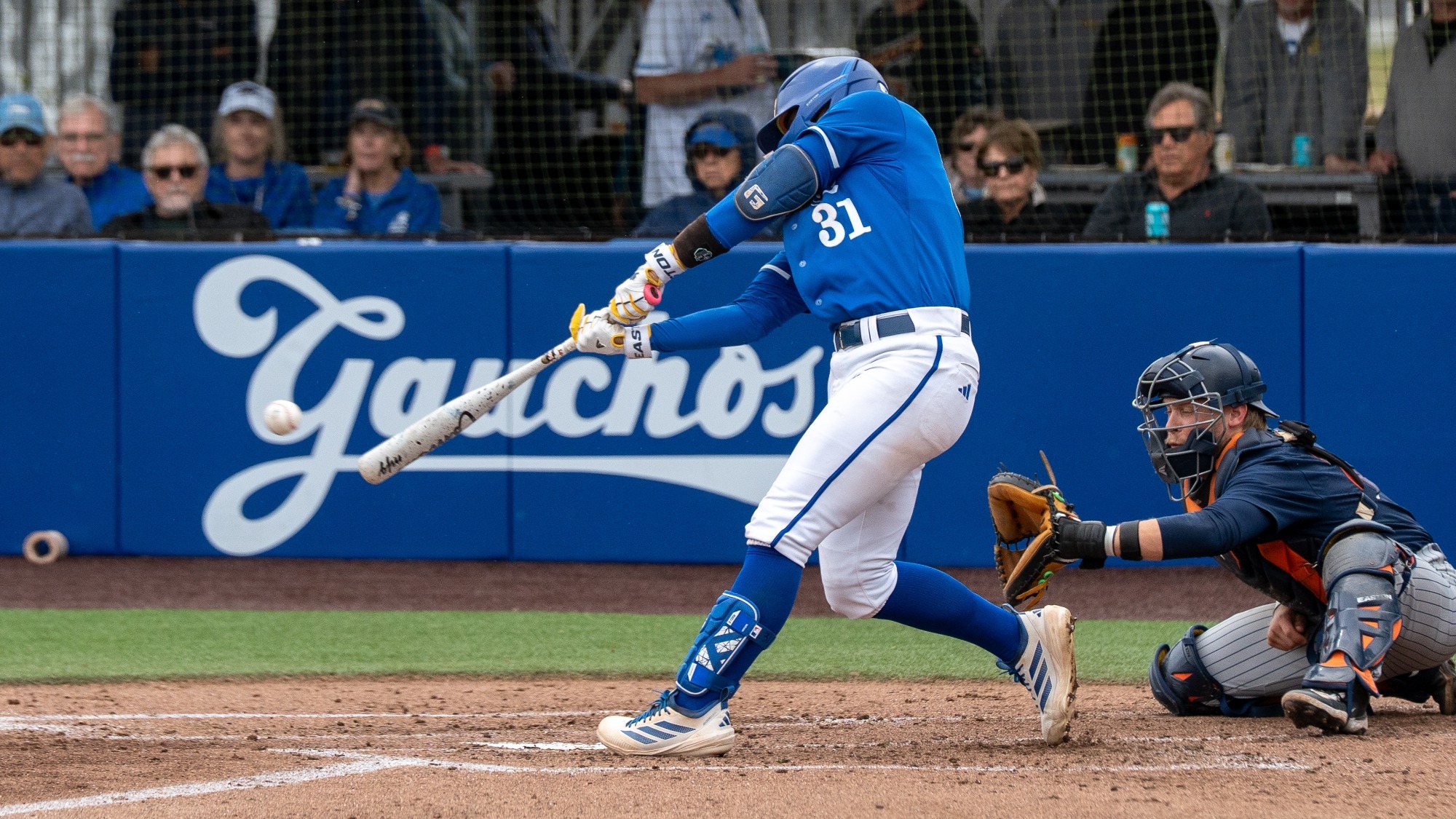 #31 Xavier Esquer swings at a low pitch on a cloudy day at Caesar Uyesaka Stadium. His arms are fully extended down and in front of his body as he reaches to connect with the ball.