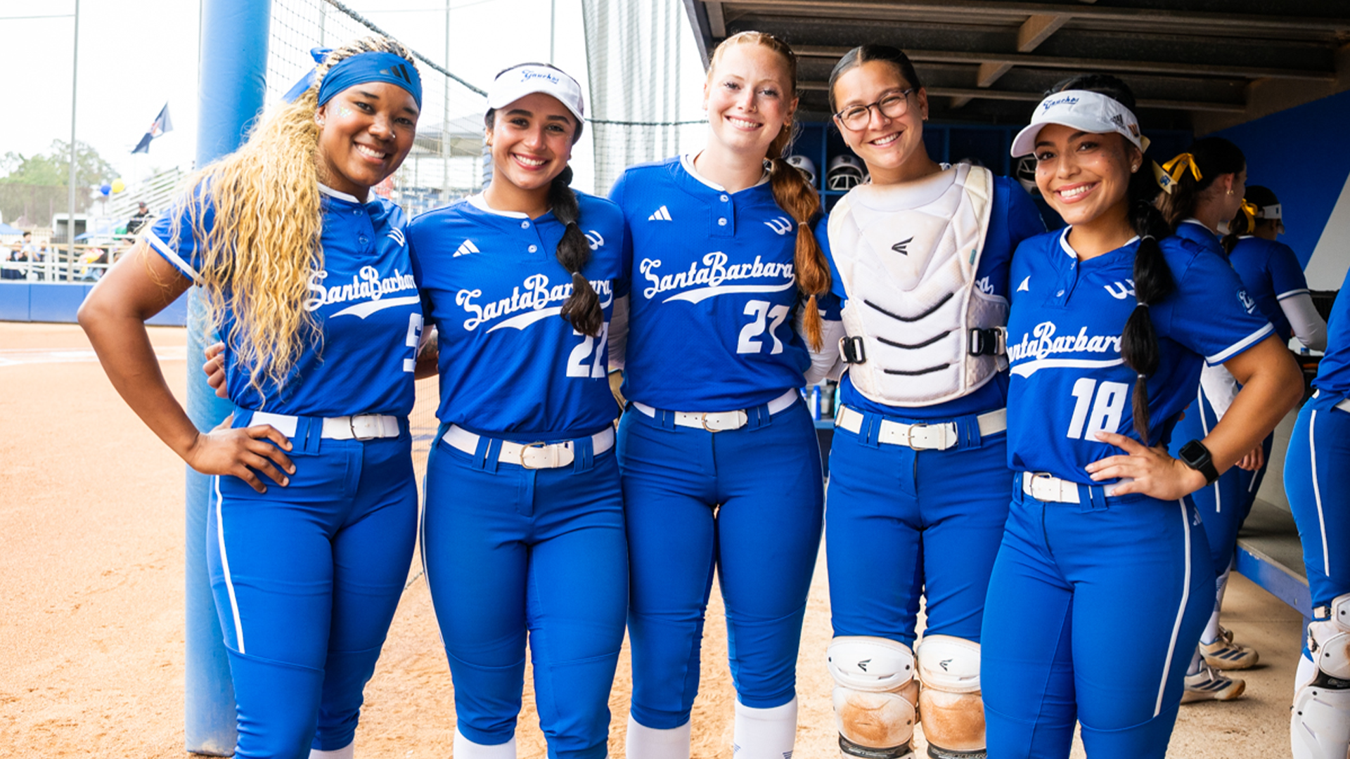 Malaya Johnson (#55), Jazzy Santos (#22), Grace Luderer (#27), Daryn Siegel (#33) and Bella Fuentes (#18) stand with their arms around each other in the UCSB dugout prior to taking the field.