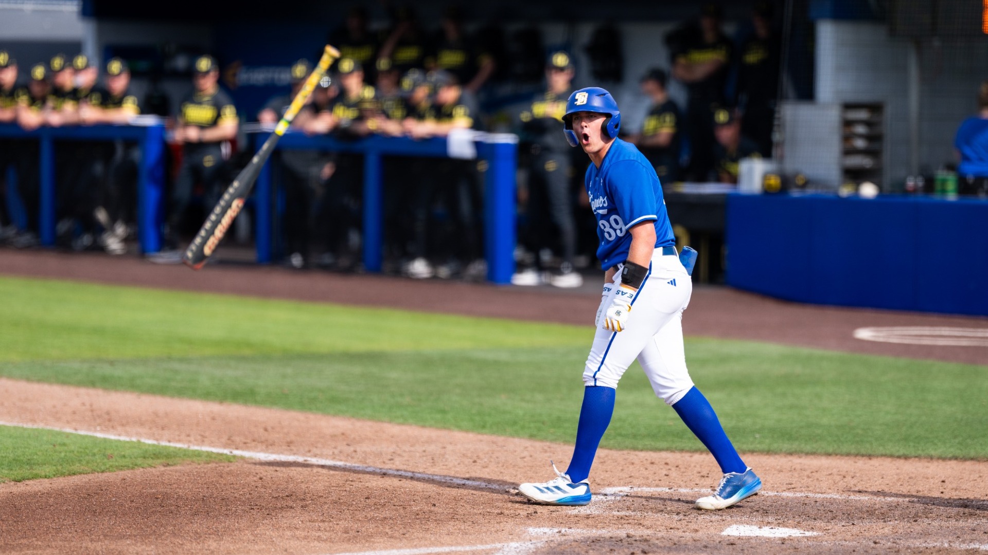#39 Mitch Namie celebrates drawing a walk against Oregon. We see him standing in the batter's box, yelling triumphantly. His bat is flying through the air towards us in the dugout, Mitch having flipped it in celebration.