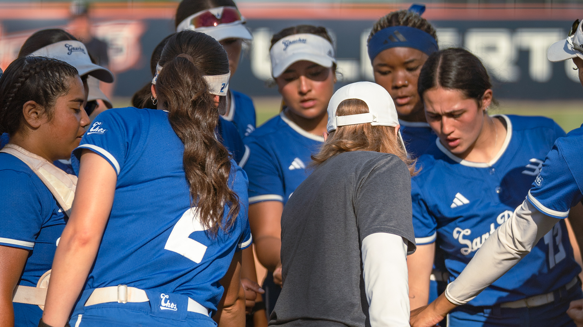 The UC Santa Barbara softball team huddles up and puts their hands in the middle of the circle for a cheer after getting off the field.