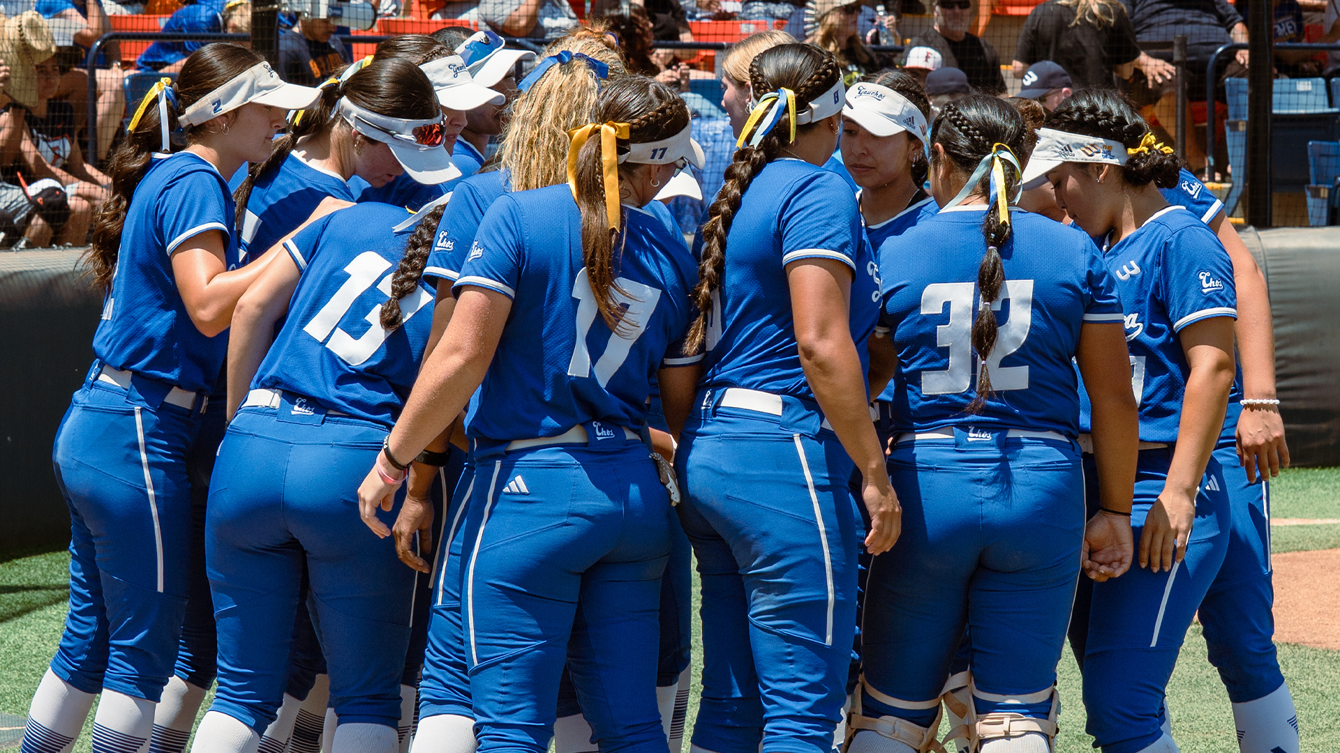 The UC Santa Barbara Softball team stands in a huddle with their hands in the center before taking the field.