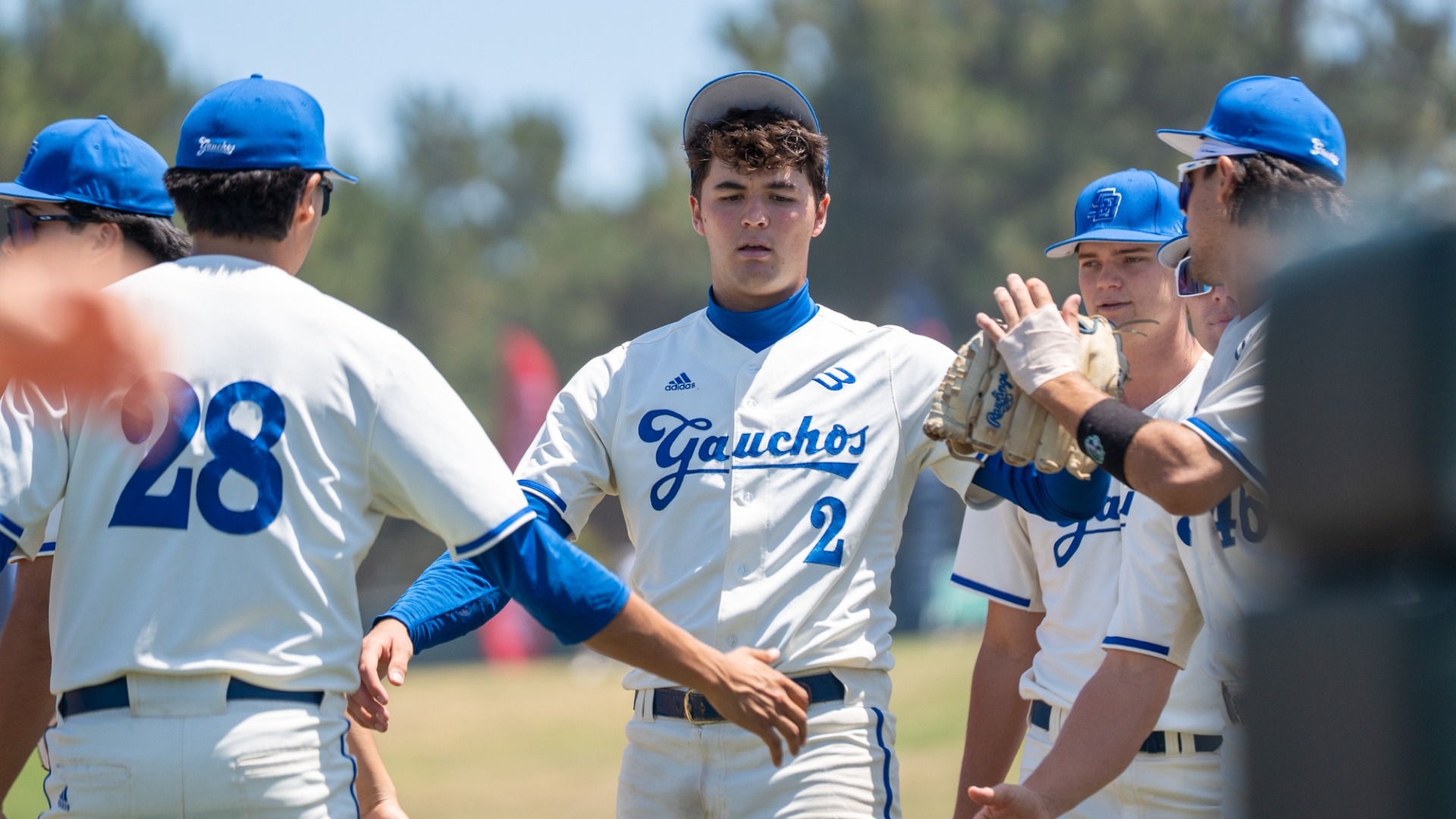 Jackson Flora receives high-fives from teammates on either side of him as he walks back into the dugout at Anteater Ballpark in Irvine