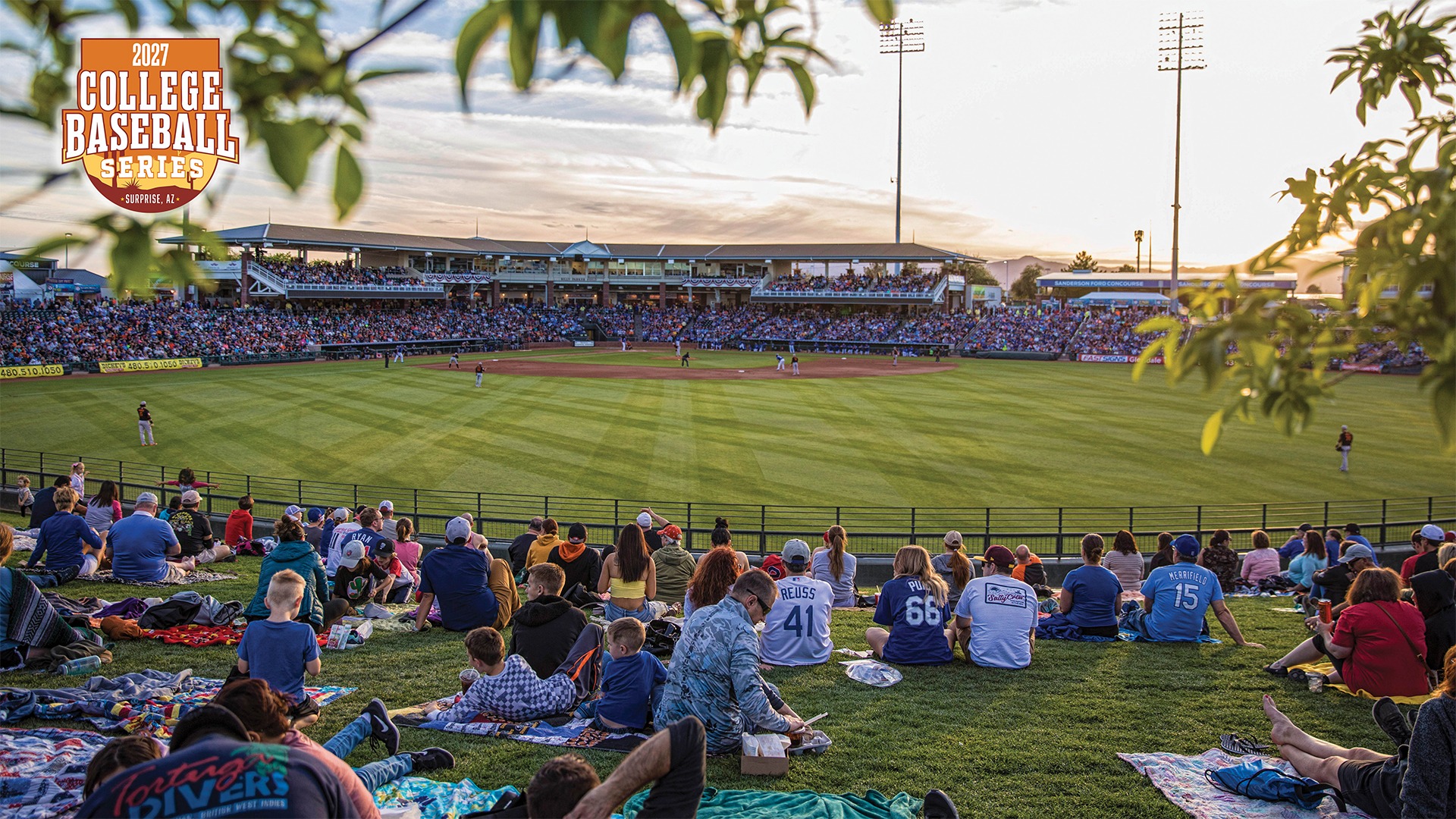 A view from the outfield lawn at Surprise Stadium during a game. Fans are spread out on the grass in the evening light. The stands are full as a game takes place on the diamond.