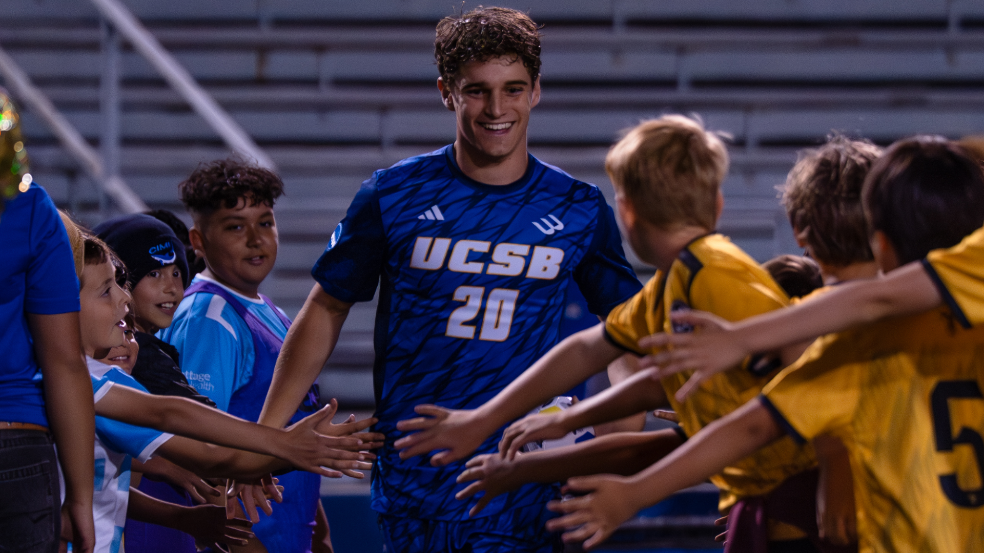 #20 Jack Middleton smiles as he makes his way down a line of young soccer players, giving out high-fives as he is introduced in the starting lineup.