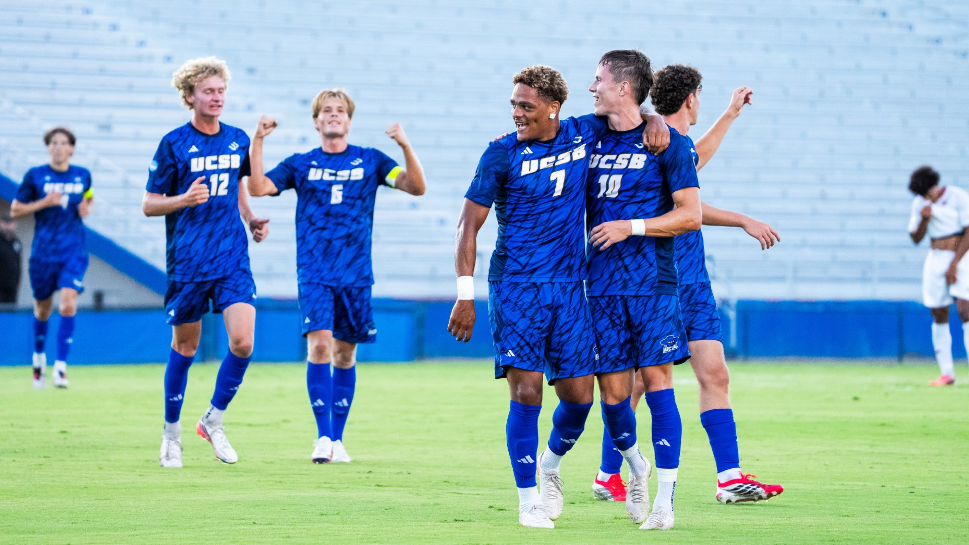 #7 Donovan Sessoms hugs #10 Steinar Bjornsson after scoring a goal. Behind them, multiple Gaucho teammates join in the celebration