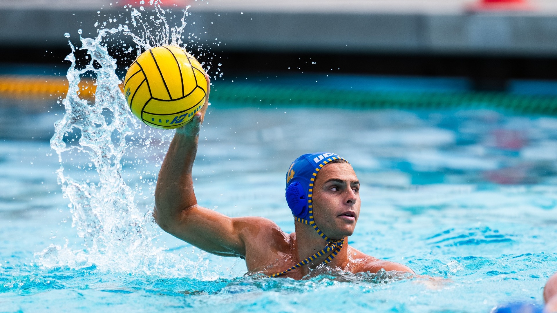Water sprays off of the ball as Dash D'Ambrosia lifts it in his right hand. Dash is looking to the left of the frame, surveying his options to pass or shoot